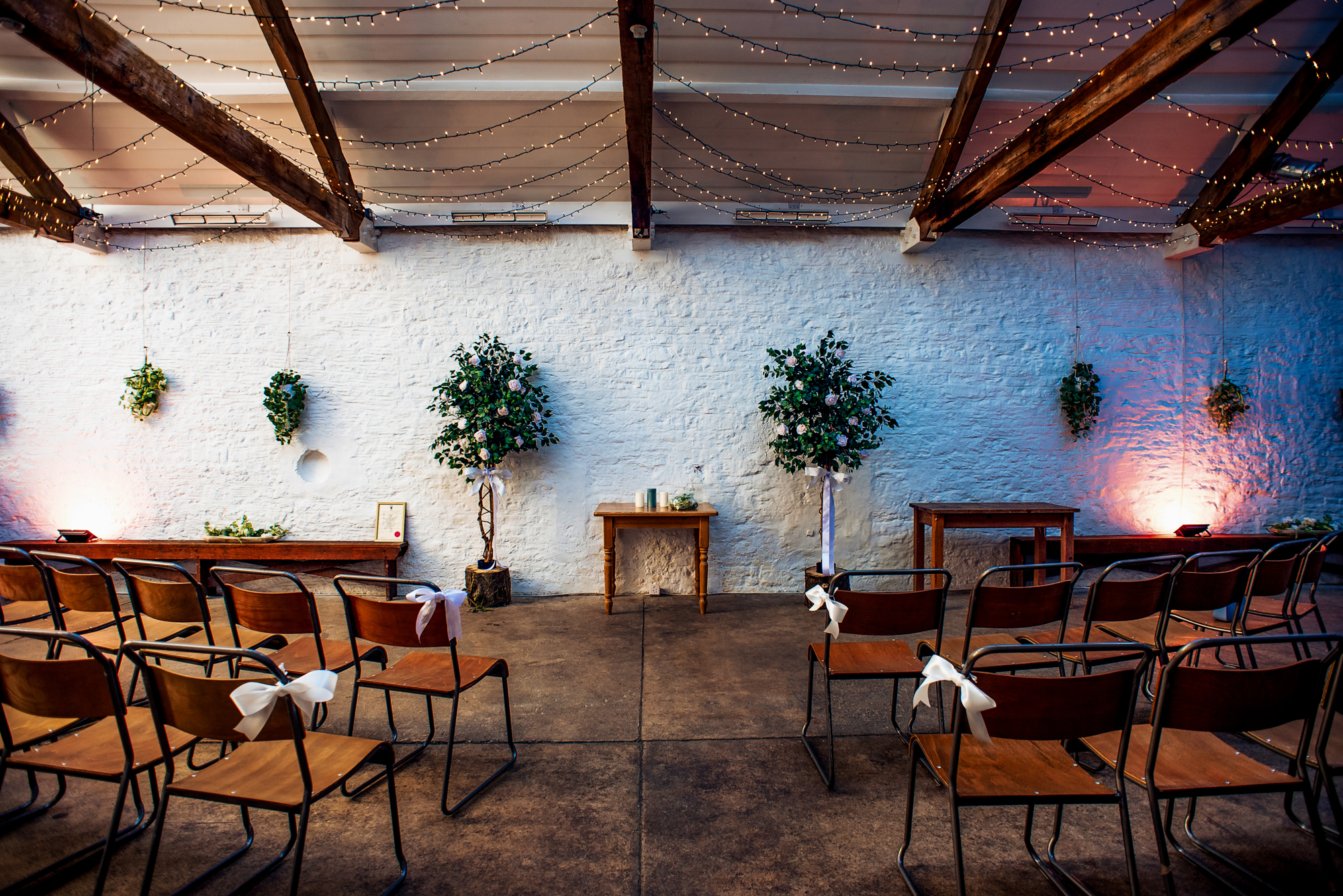 Ceremony space at Silk Mill Studios in Frome with wooden chairs, white stone walls, and fairy lights.