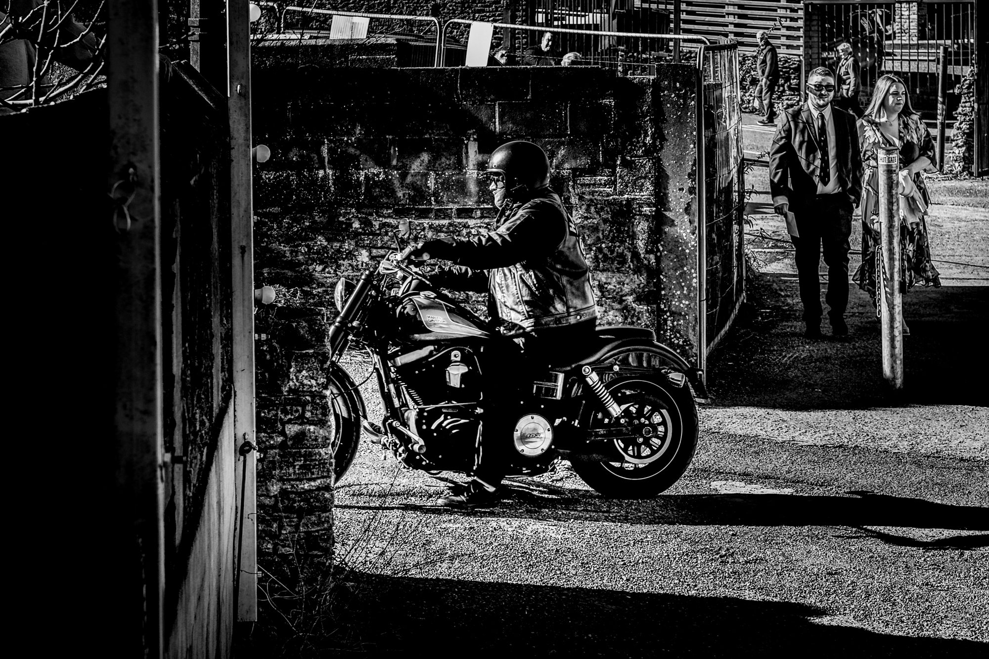 Motorbike rider arriving as wedding guests walk into the courtyard at Silk Mill Studios.