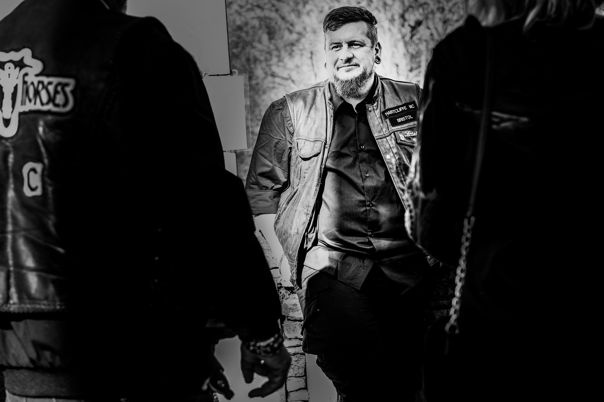 Man in Hartcliffe MC Bristol cut standing outdoors with motorcycle club members around him.