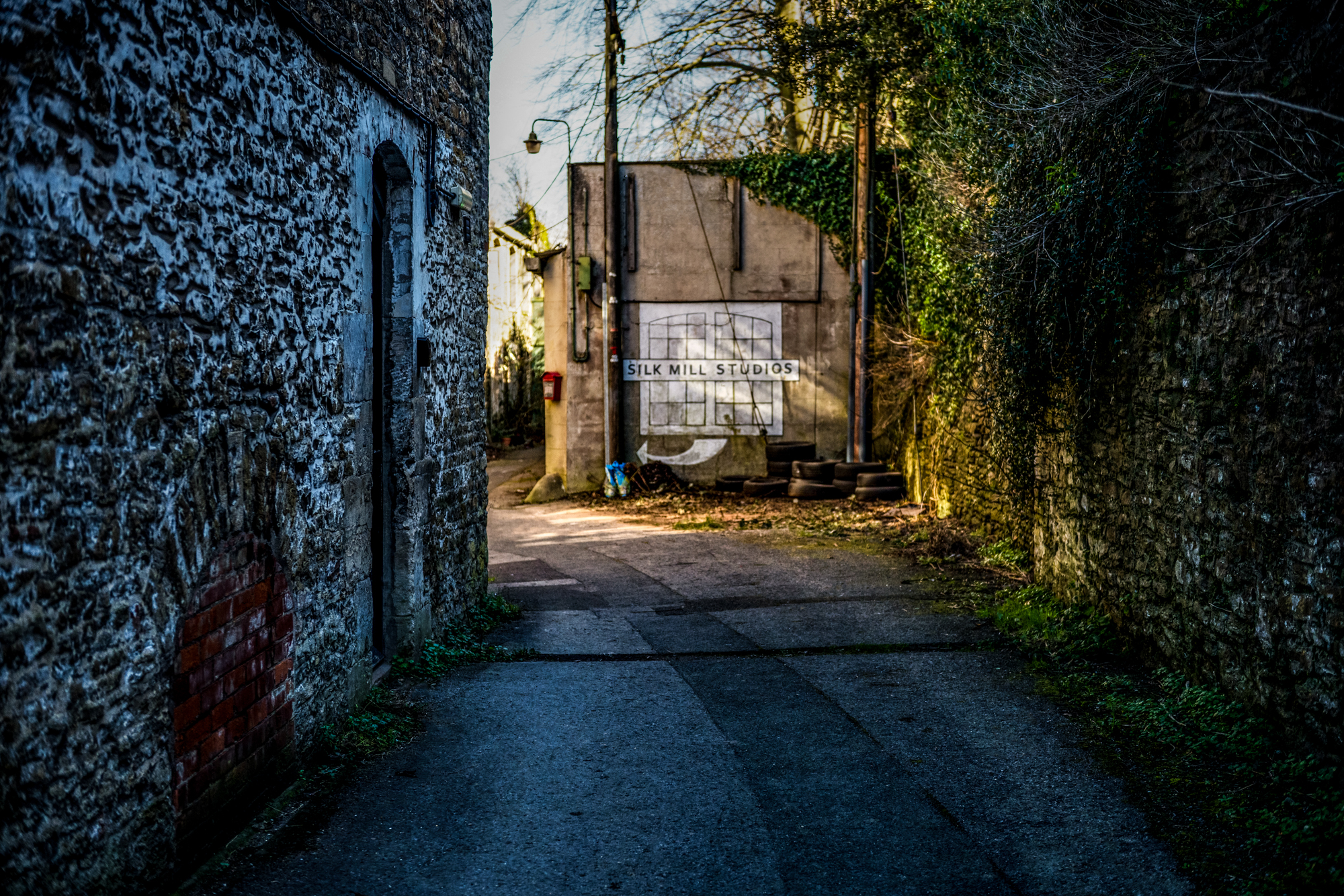 Narrow lane leading to Silk Mill Studios sign between old stone buildings in Frome.