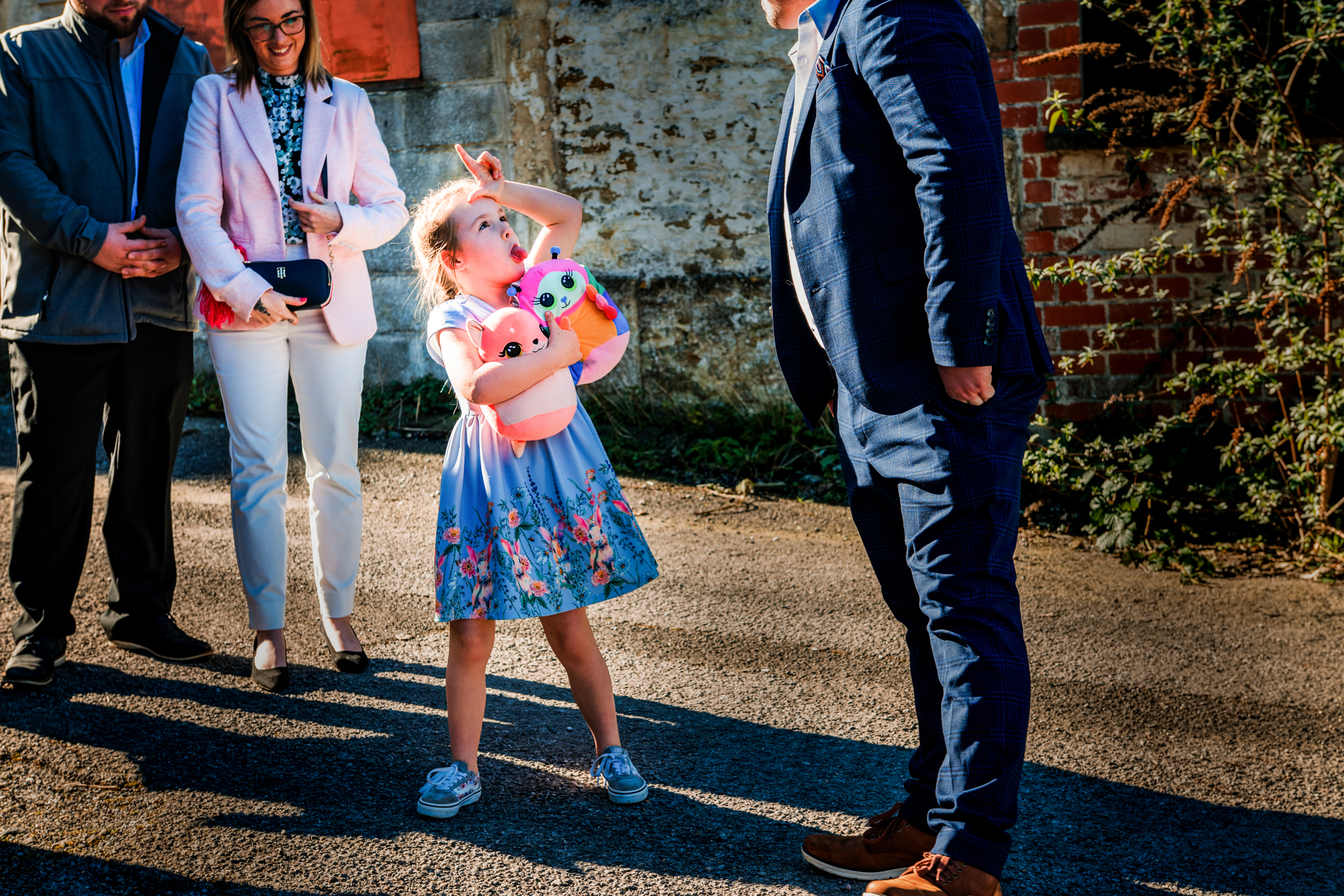 Young wedding guest holding soft toys and pulling a funny face outside the venue.