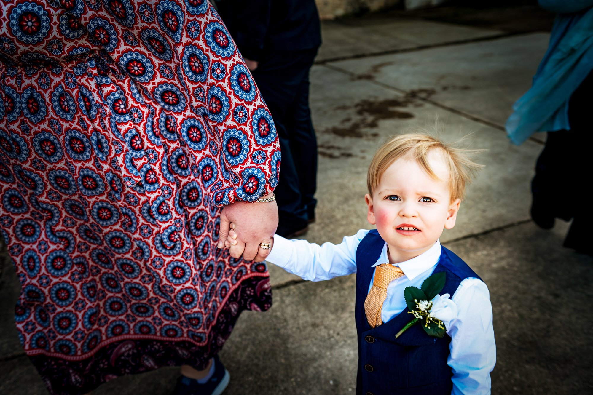 Little boy in a blue waistcoat holding an adult’s hand during the wedding celebration.