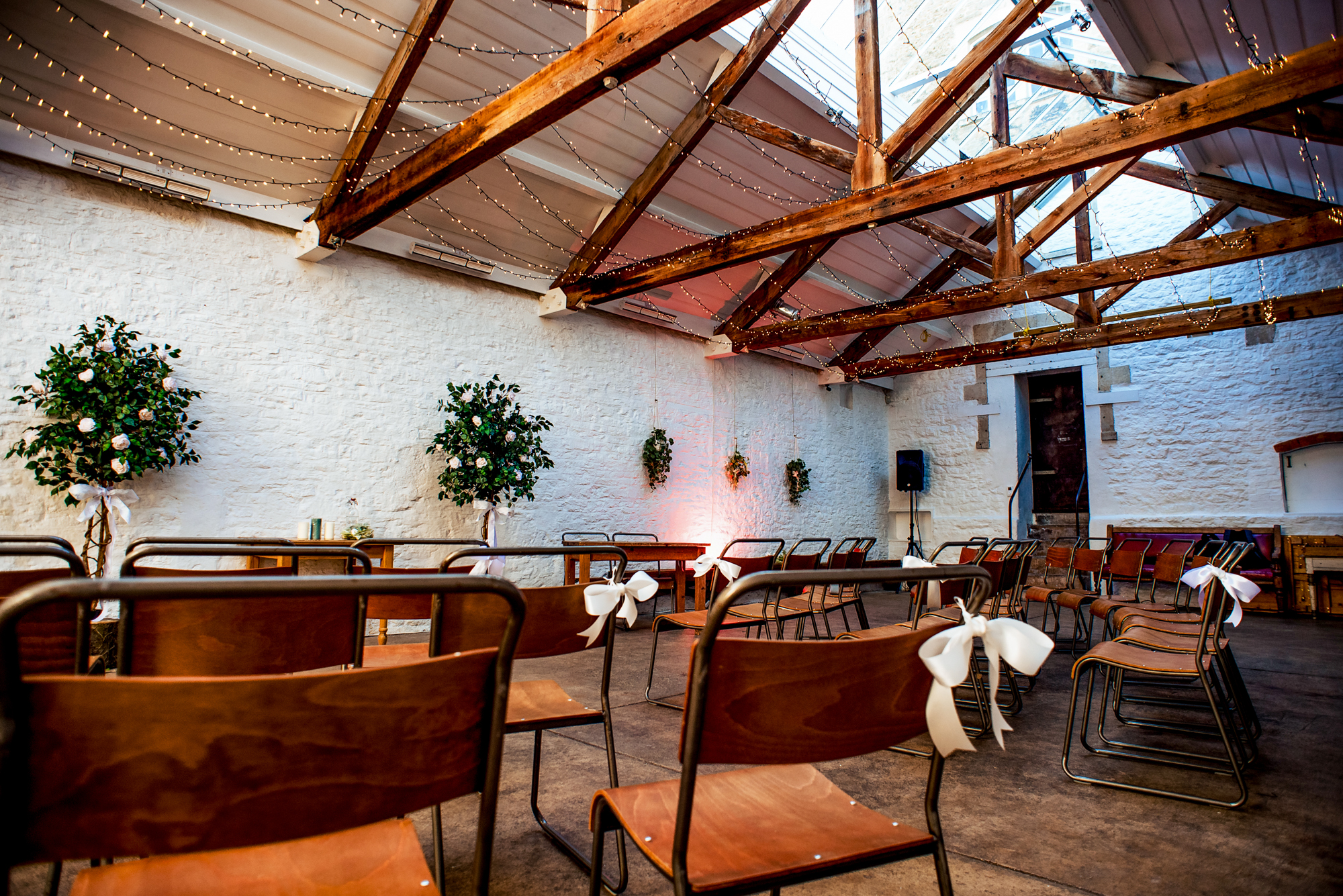 Wedding ceremony room at Silk Mill Studios with exposed beams, skylights, and chairs tied with white bows.