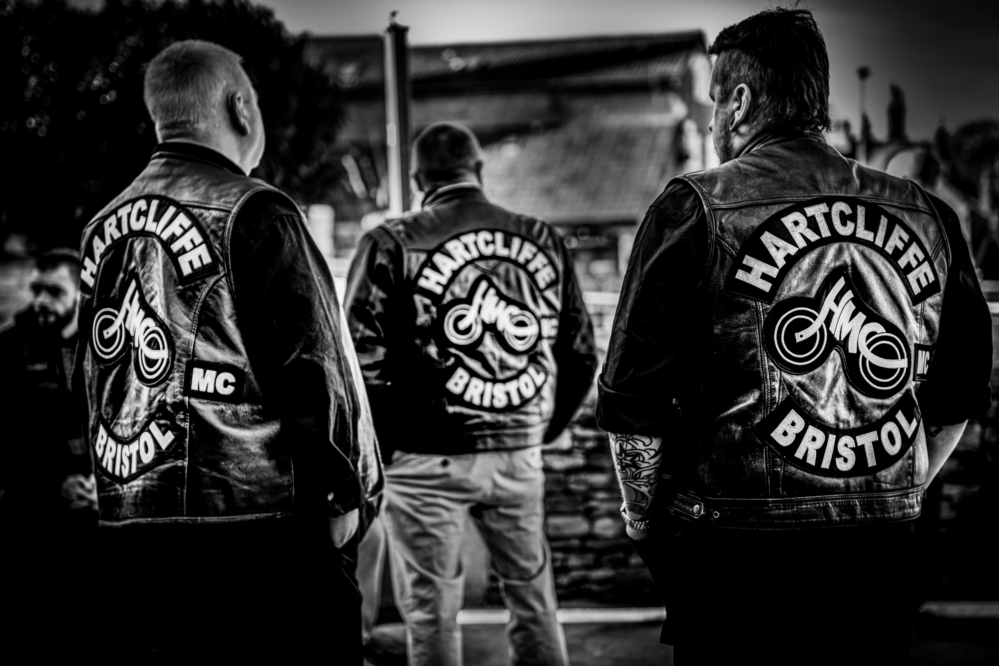 Three Hartcliffe MC Bristol members stand together in leather cuts during the wedding celebration.