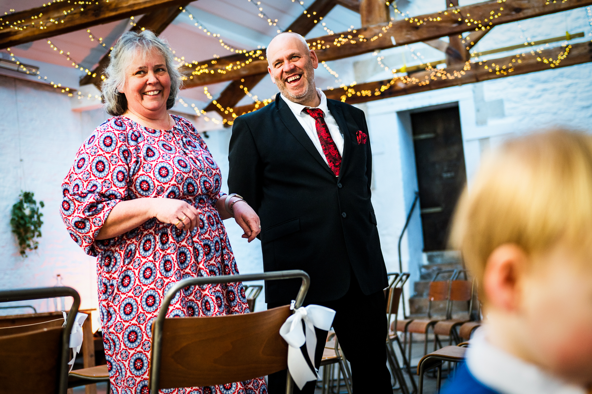 Two guests smile beside the ceremony chairs under fairy lights at Silk Mill Studios.
