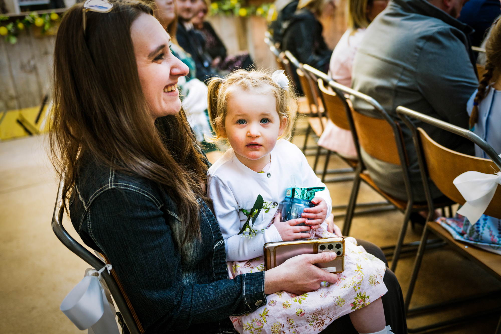 A woman smiles while a little girl sits on her lap holding a blue cup.