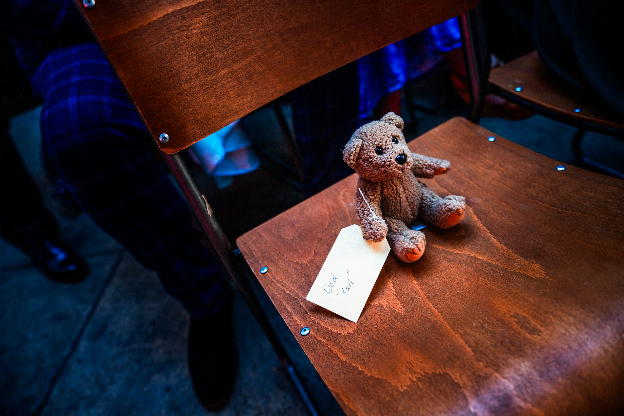 A teddy bear with a handwritten tag sits quietly on a wooden ceremony chair.