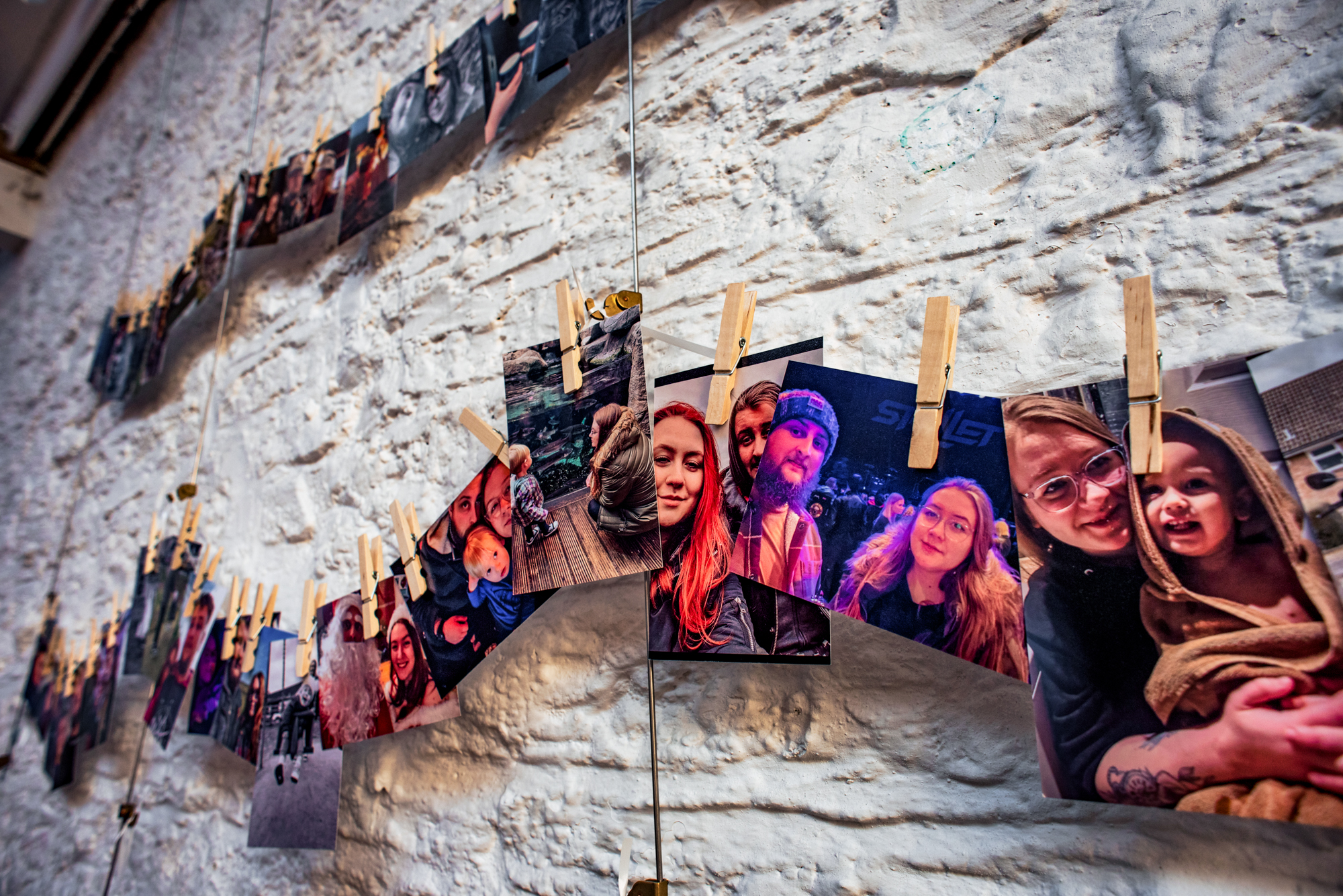 Printed family photos clipped to strings against a white stone wall at Silk Mill Studios.