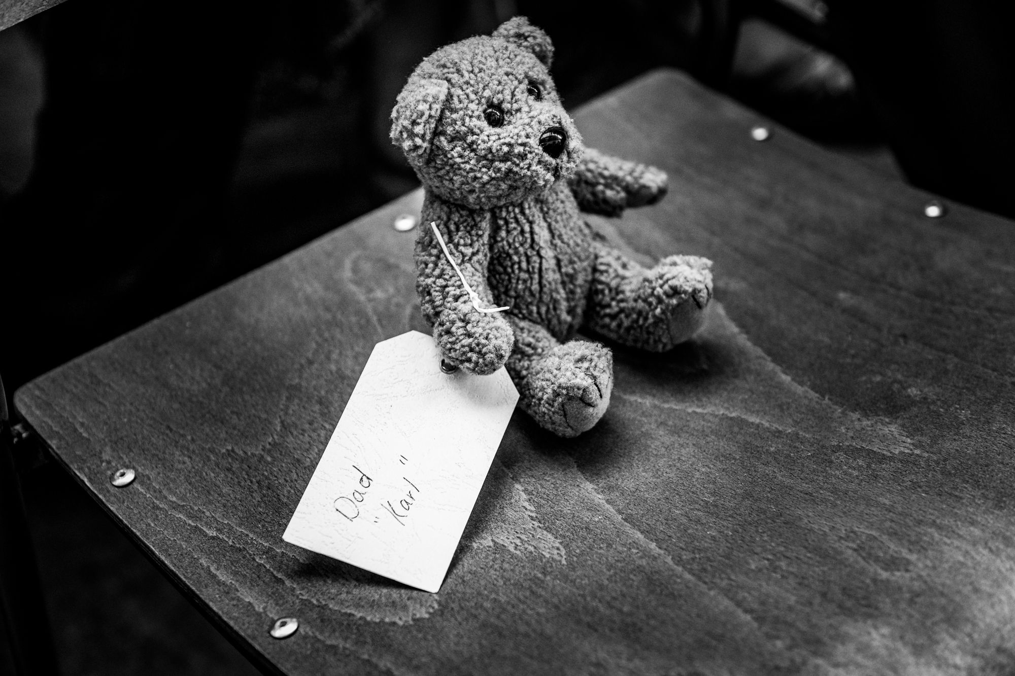 A teddy bear with a handwritten tag reading Dad Karl sits on a chair.