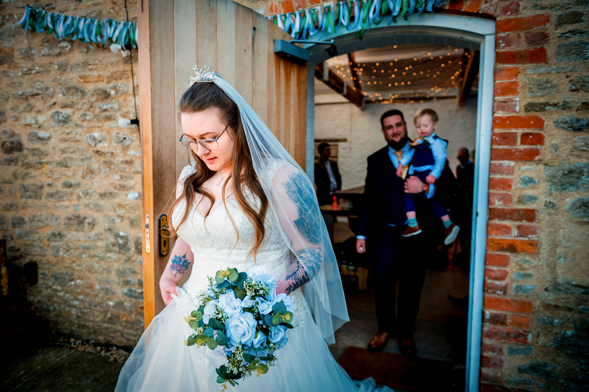 Nat steps through the doorway holding her bouquet as Jon follows carrying Theo.
