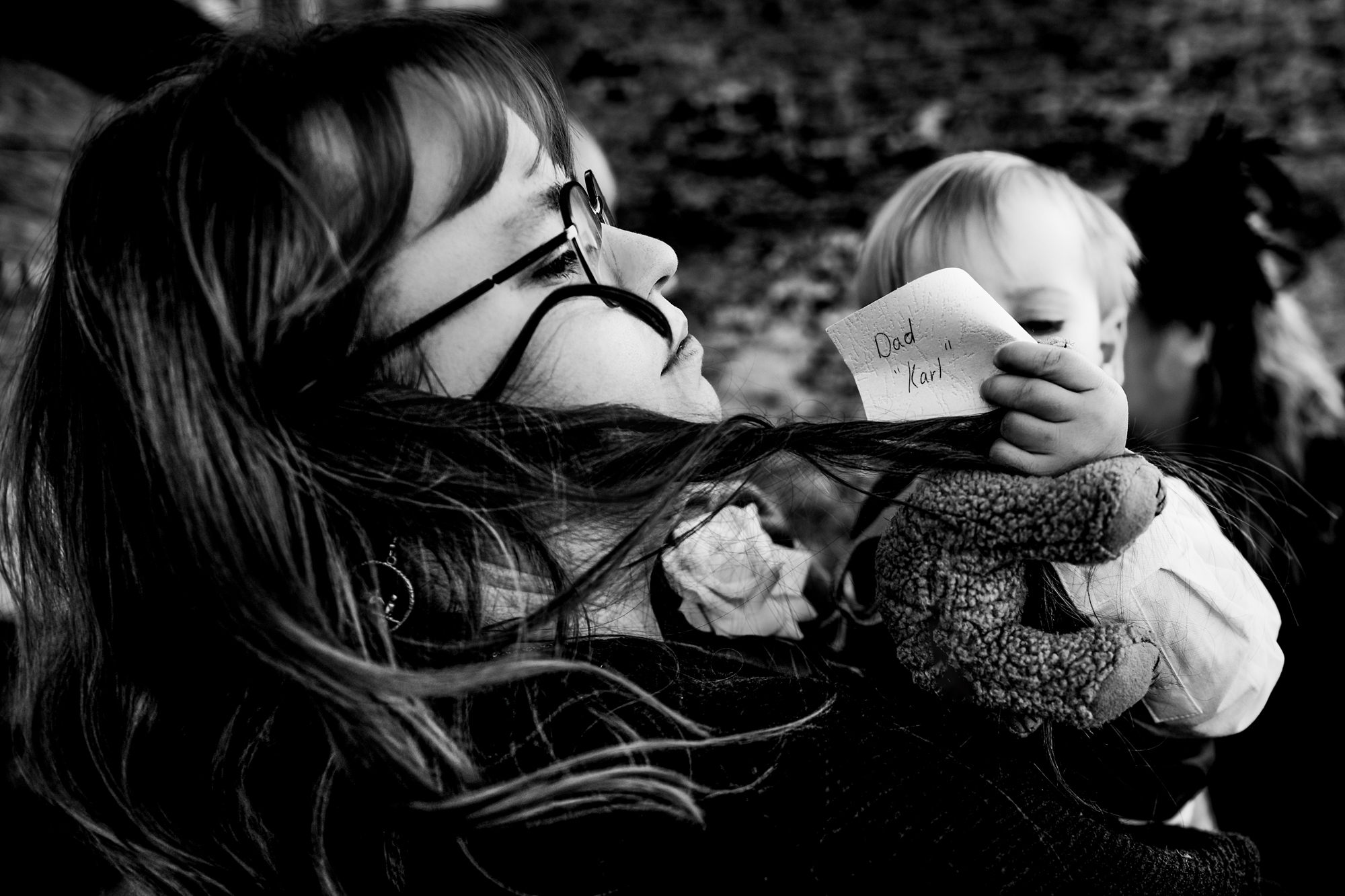 A child holds the Dad Karl tag and teddy bear during an emotional family moment.
