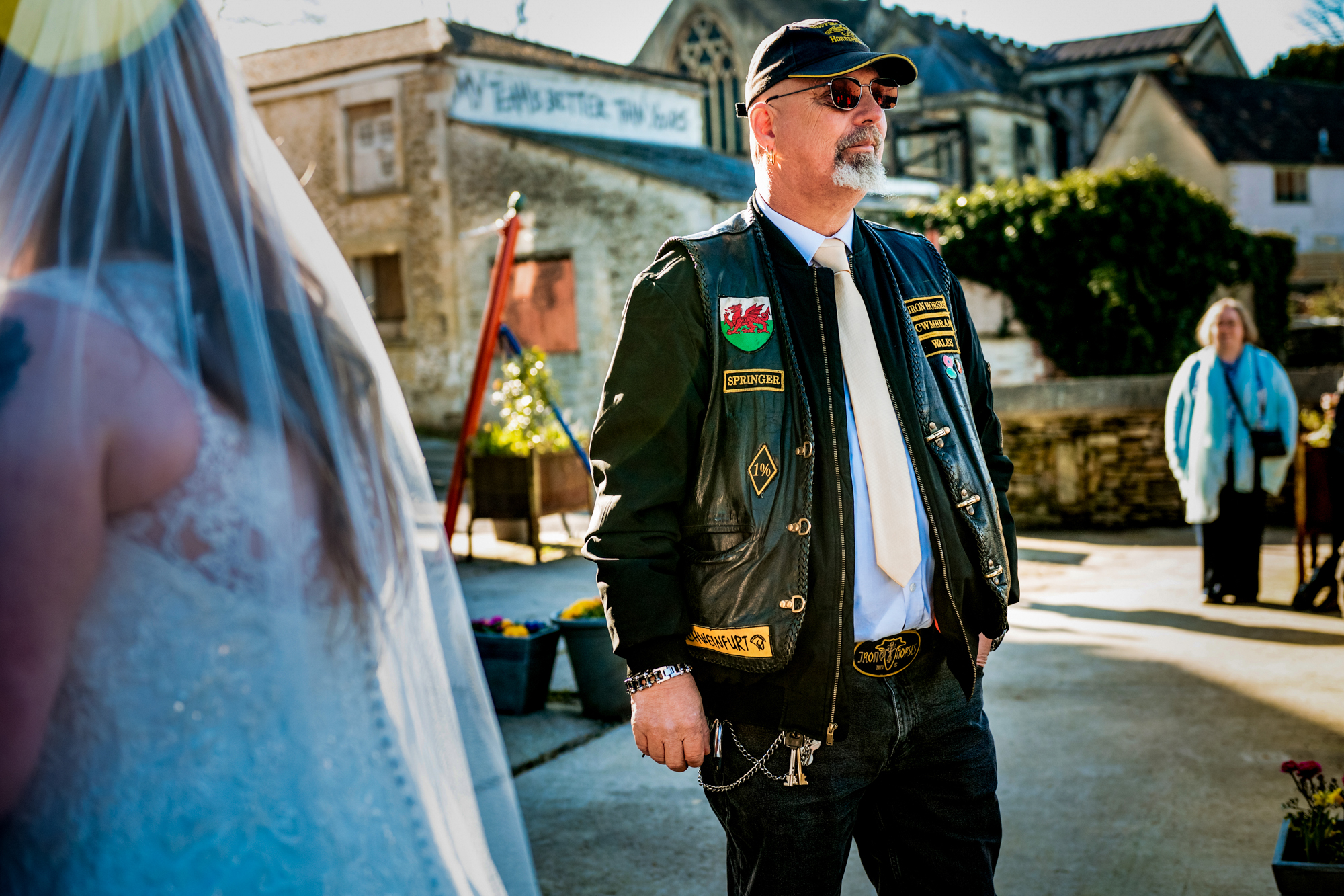 Wedding guest in a leather vest stands in the courtyard after the ceremony.