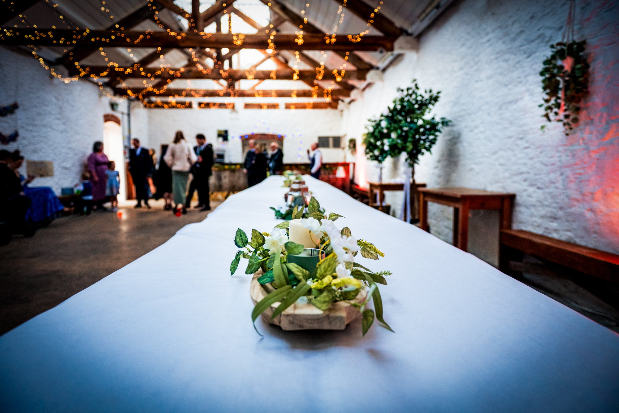 Long banquet table set inside Silk Mill Studios with greenery, candles, and fairy lights overhead.