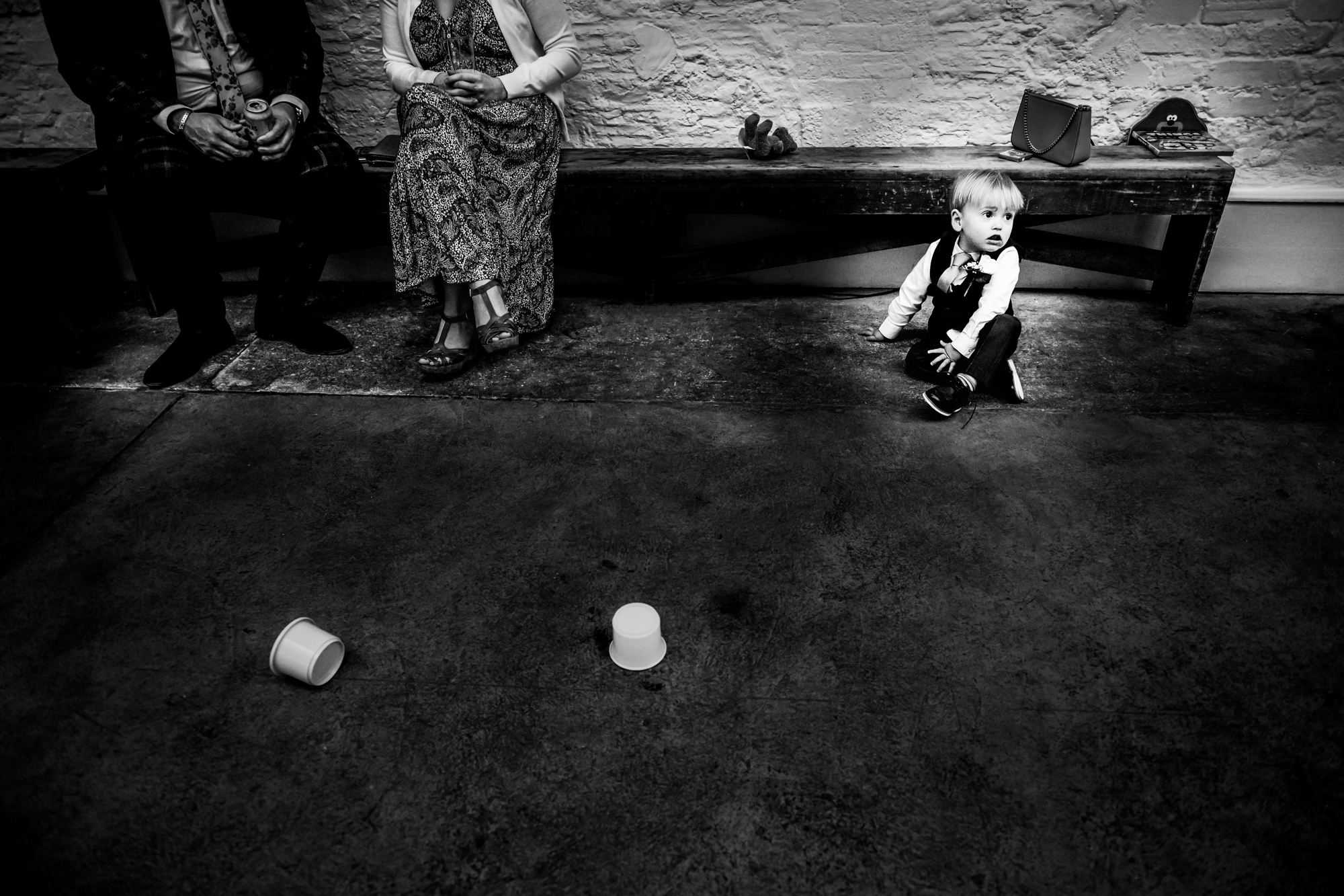 Little boy sits on the floor near two paper cups during the wedding reception.