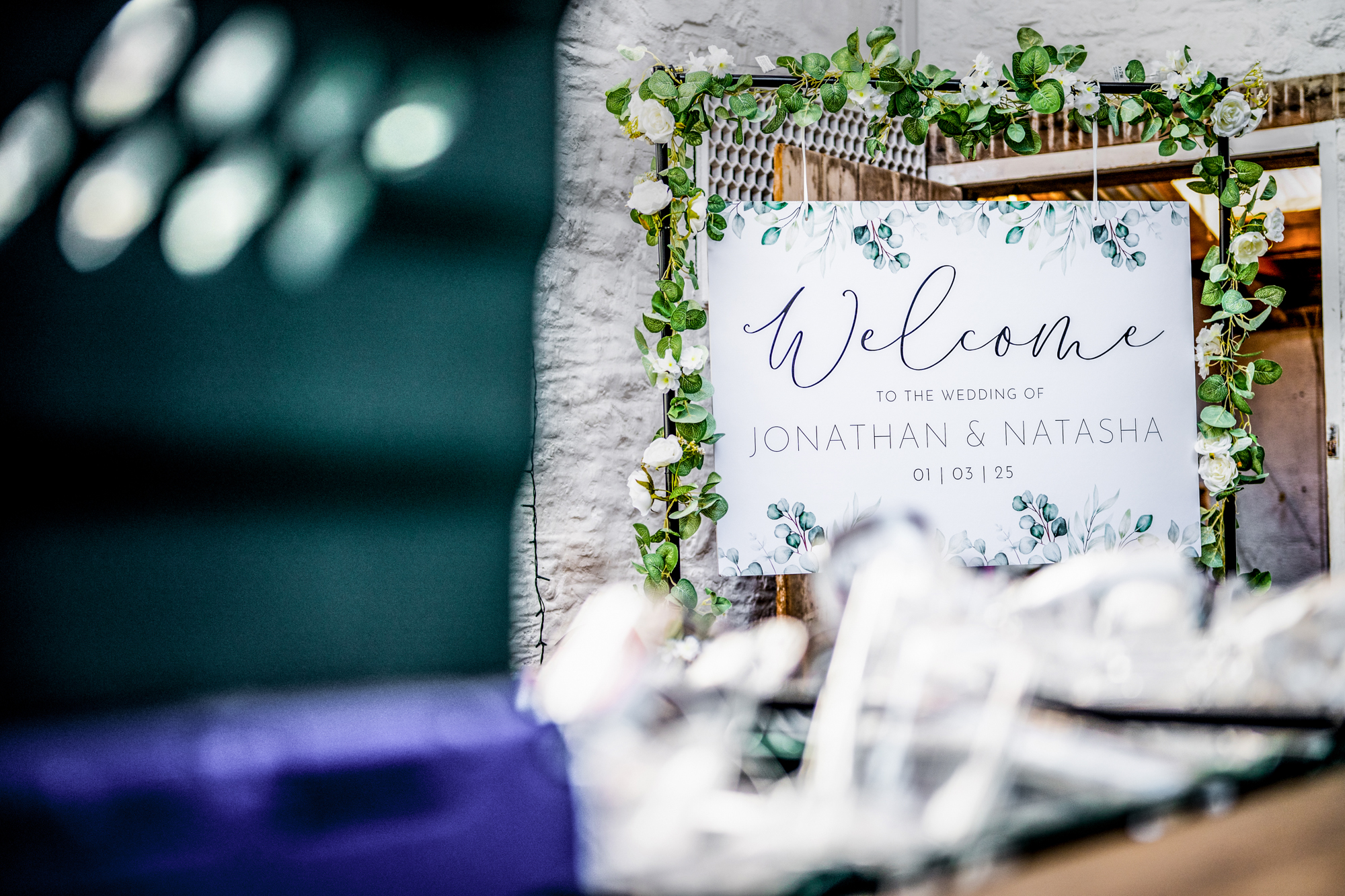 Welcome sign for Jonathan and Natasha’s wedding framed with greenery inside Silk Mill Studios.