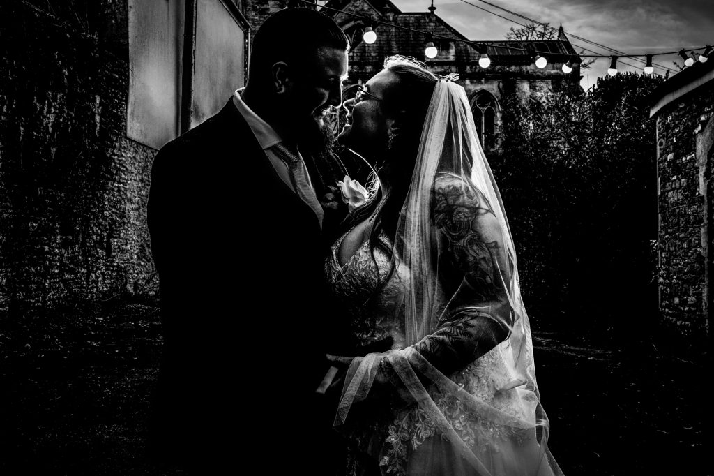 Black and white silhouette of Nat and Jon smiling at each other beneath festoon lights.