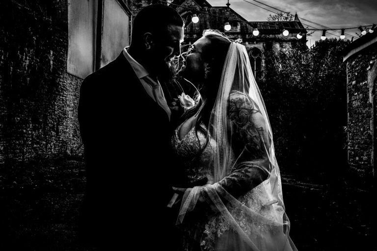 Black and white silhouette of Nat and Jon smiling at each other beneath festoon lights.