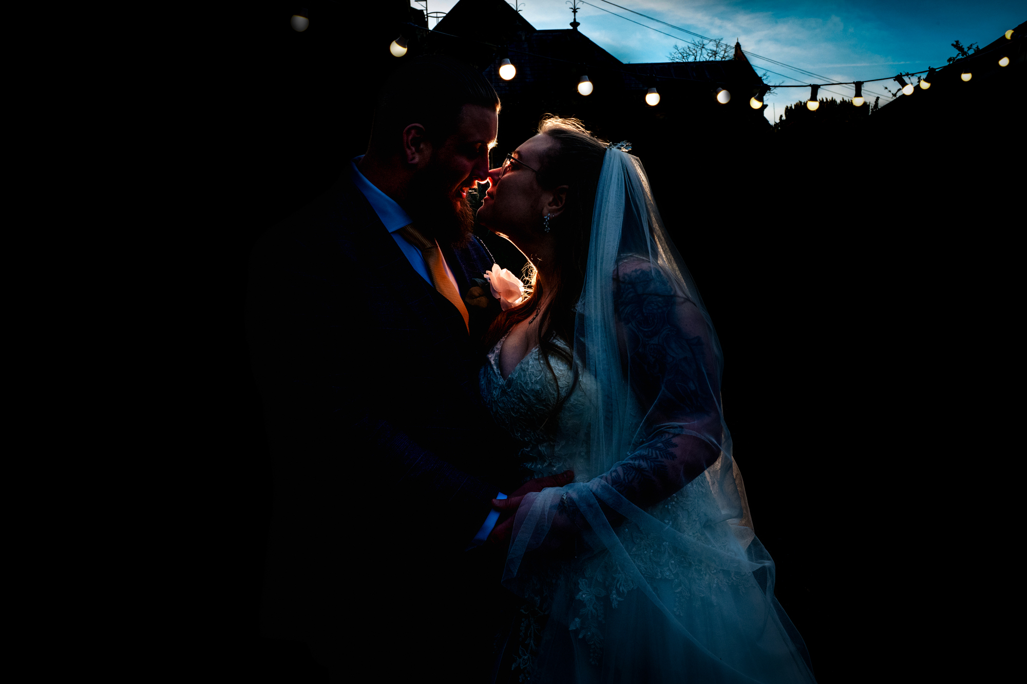 Nat and Jon lean close in a dramatic backlit portrait outside Silk Mill Studios.