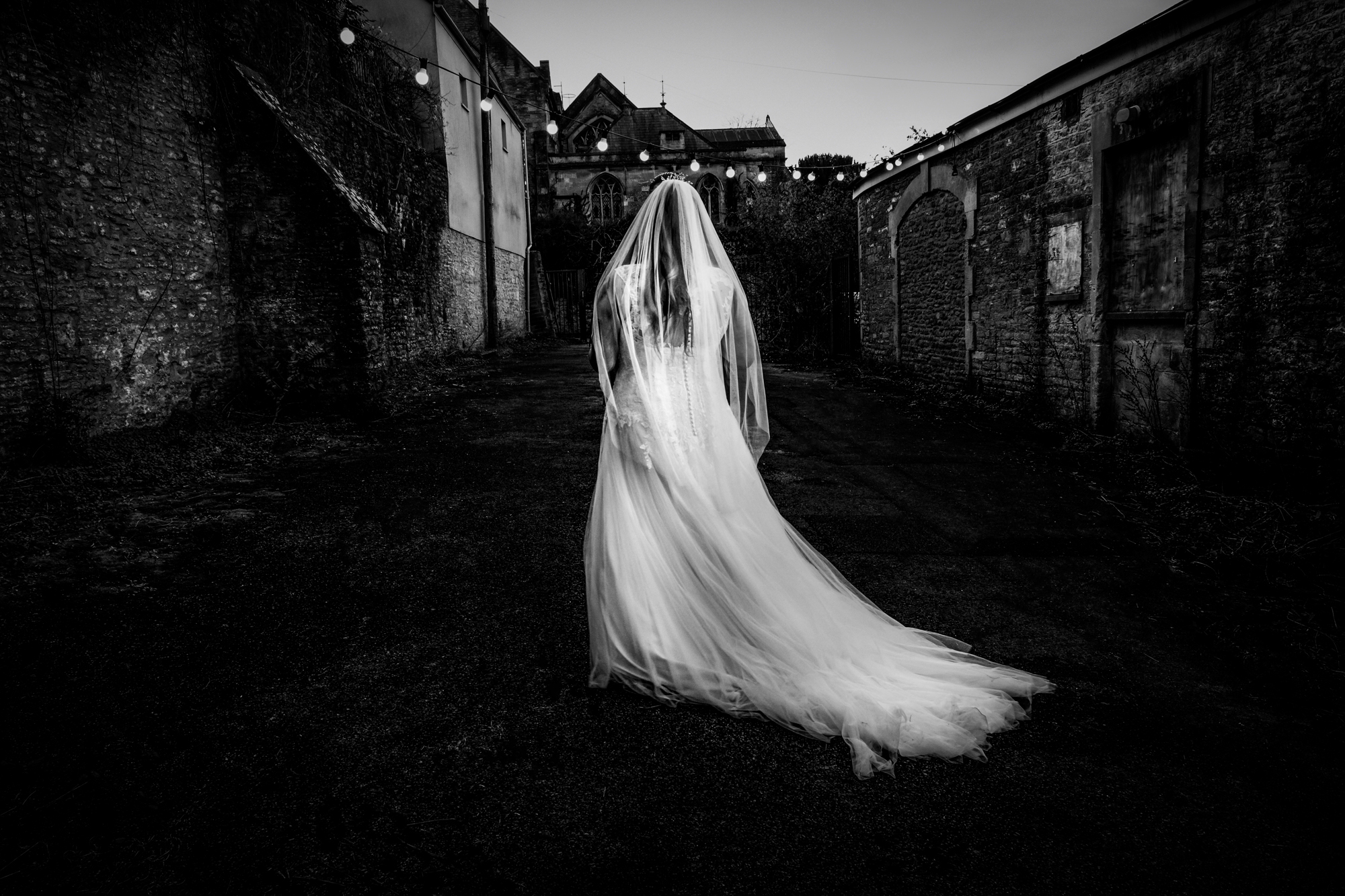 Nat walks alone through the alley outside Silk Mill Studios with her veil trailing behind.