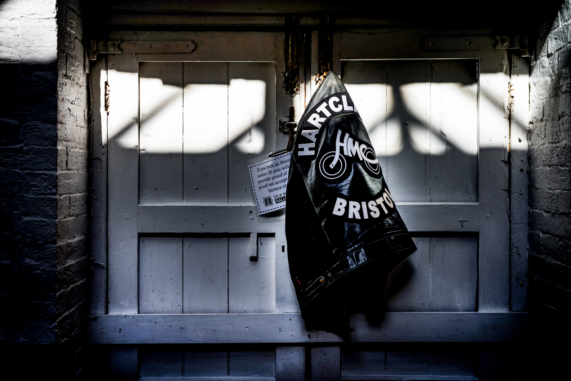 Hartcliffe MC Bristol leather jacket hanging against weathered doors at Silk Mill Studios.