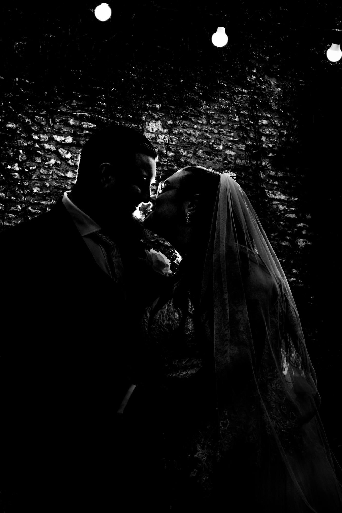 Silhouette of Nat and Jon kissing beneath festoon lights outside Silk Mill Studios.