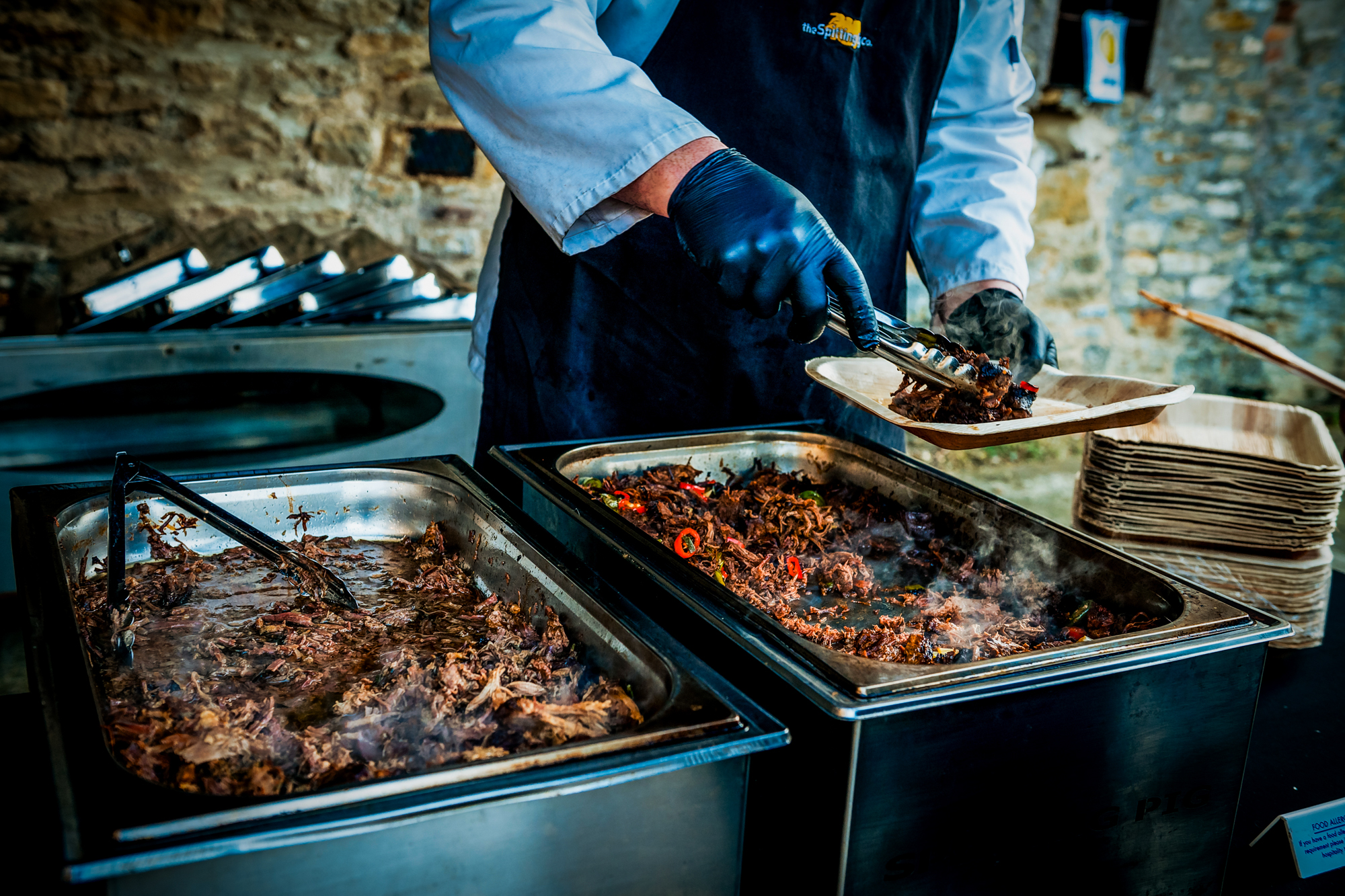 Caterer serves hot pulled pork from the Spitting Pig buffet onto a plate.