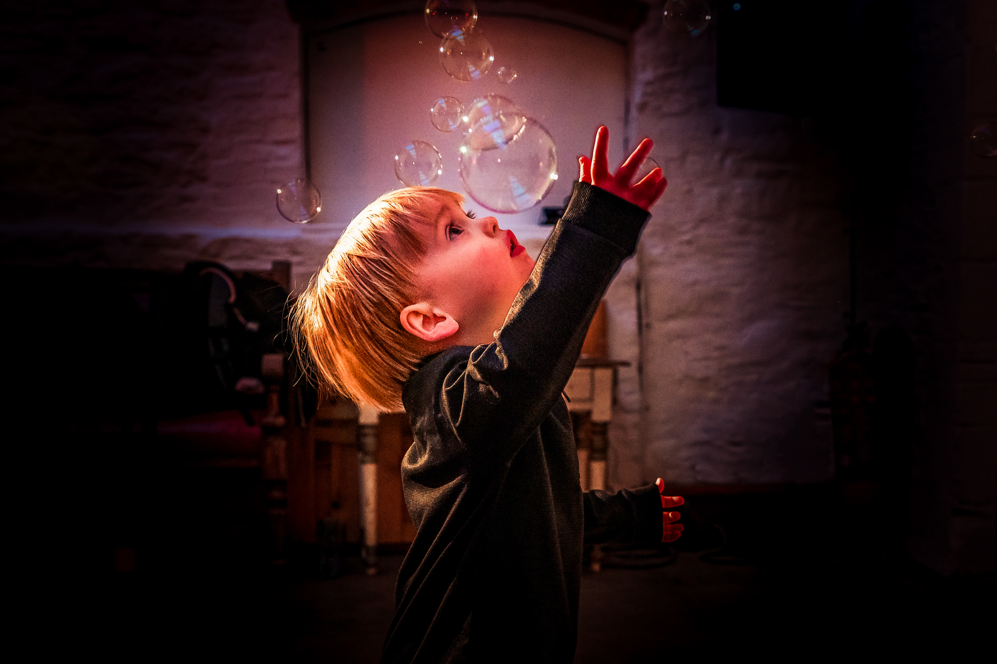 Little boy reaches up toward floating bubbles on the dance floor at the wedding.