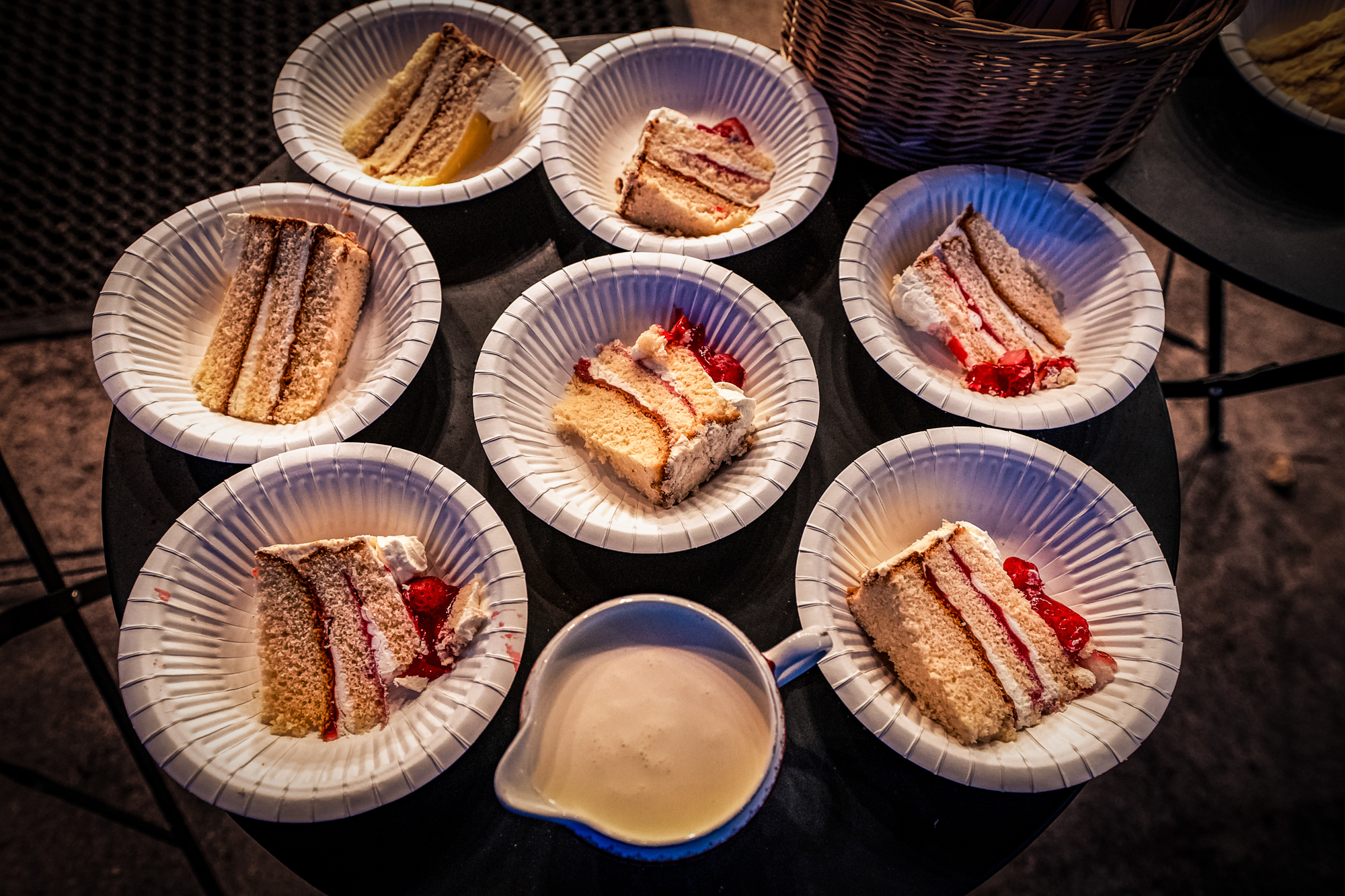 Close-up of black forest gateau slices on paper plates beside a jug of cream.
