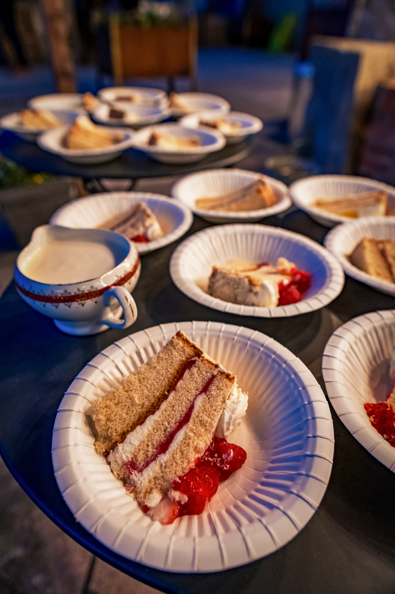 Slices of black forest gateau served on paper plates with a jug of cream.