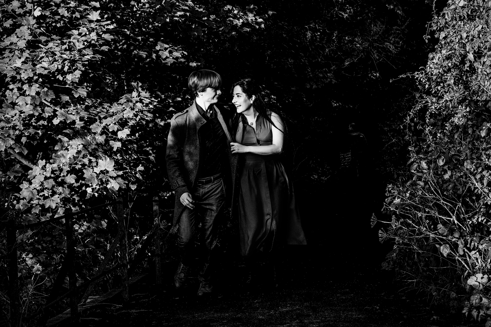 Couple walking through shadowy woodland path during Clifton engagement shoot in dramatic evening light.