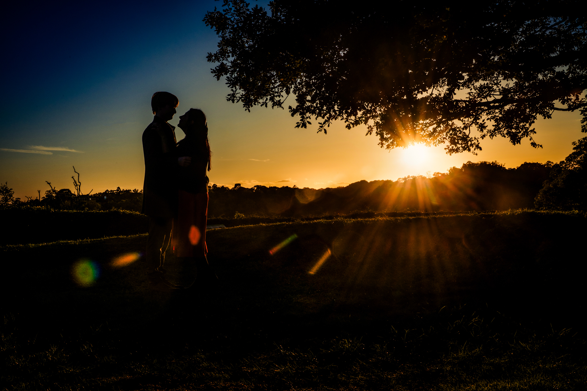 Couple silhouetted against golden sunset sky during romantic outdoor engagement session in Clifton.