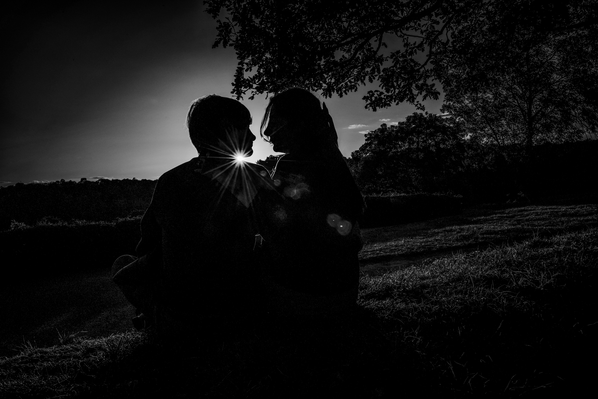 Black and white silhouette of couple sitting closely with starburst light behind them.
