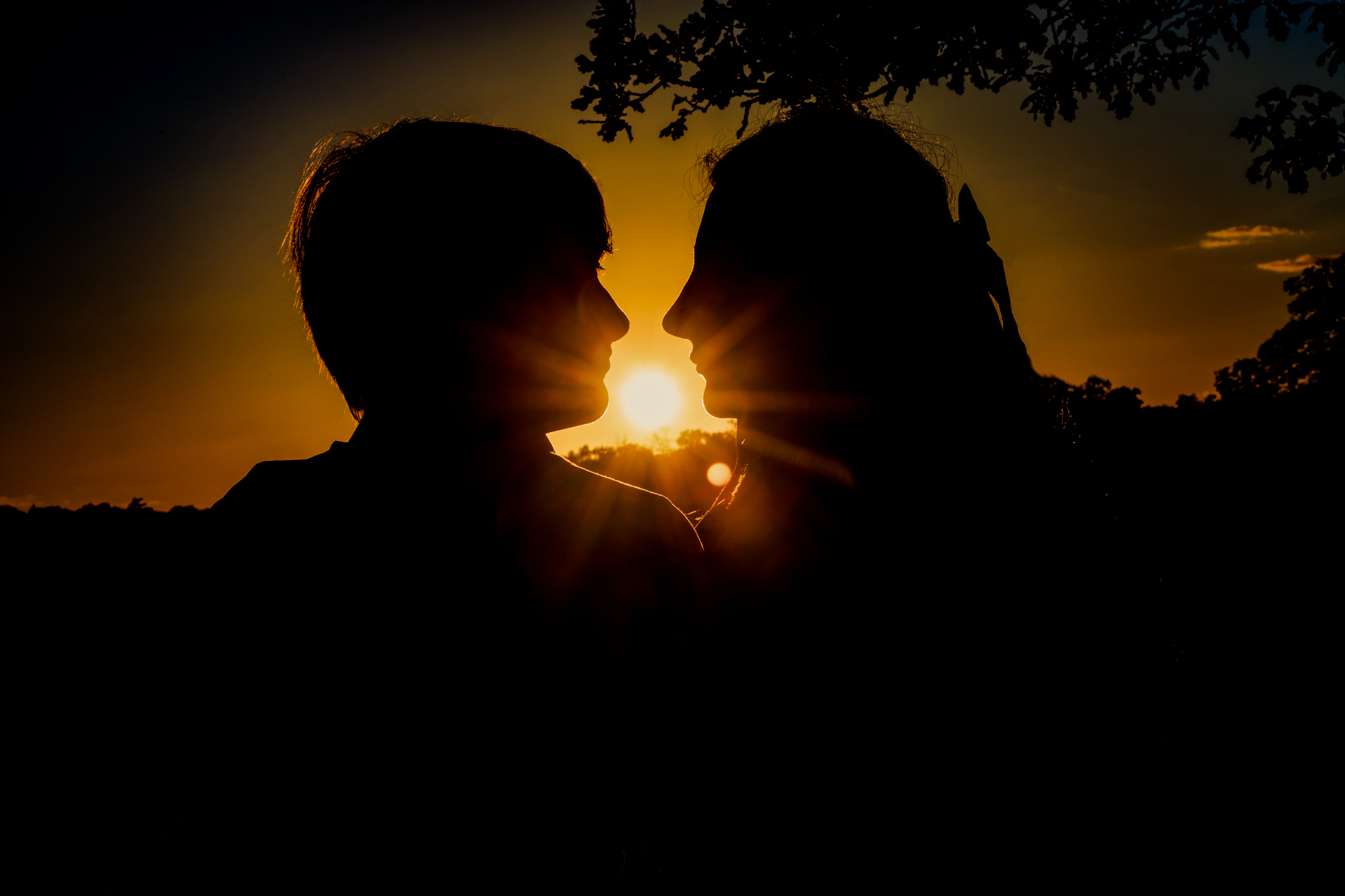 Silhouetted couple facing each other with glowing sunset behind them in Clifton park.