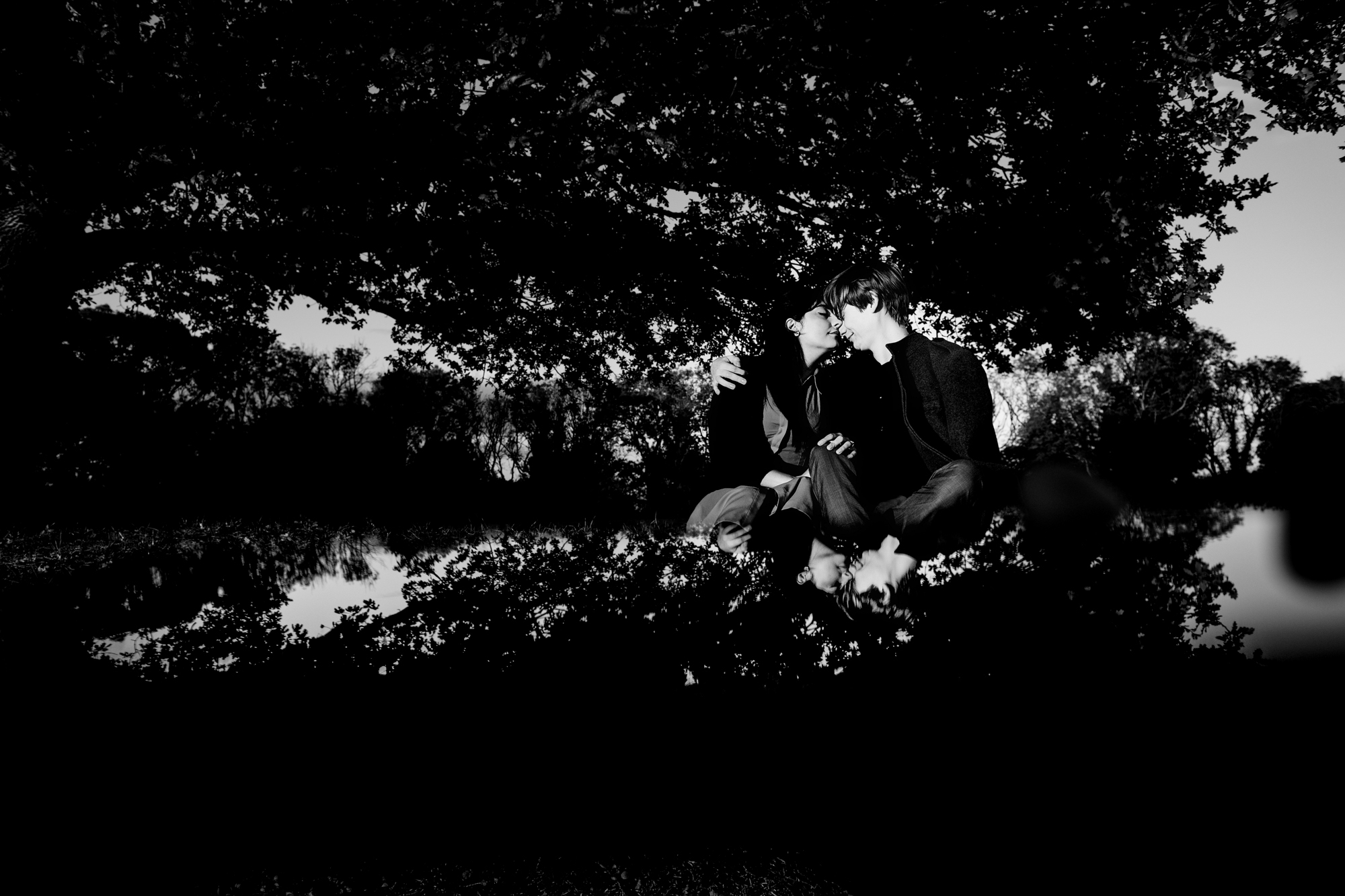 Black and white portrait of couple sitting beneath tree with reflection.