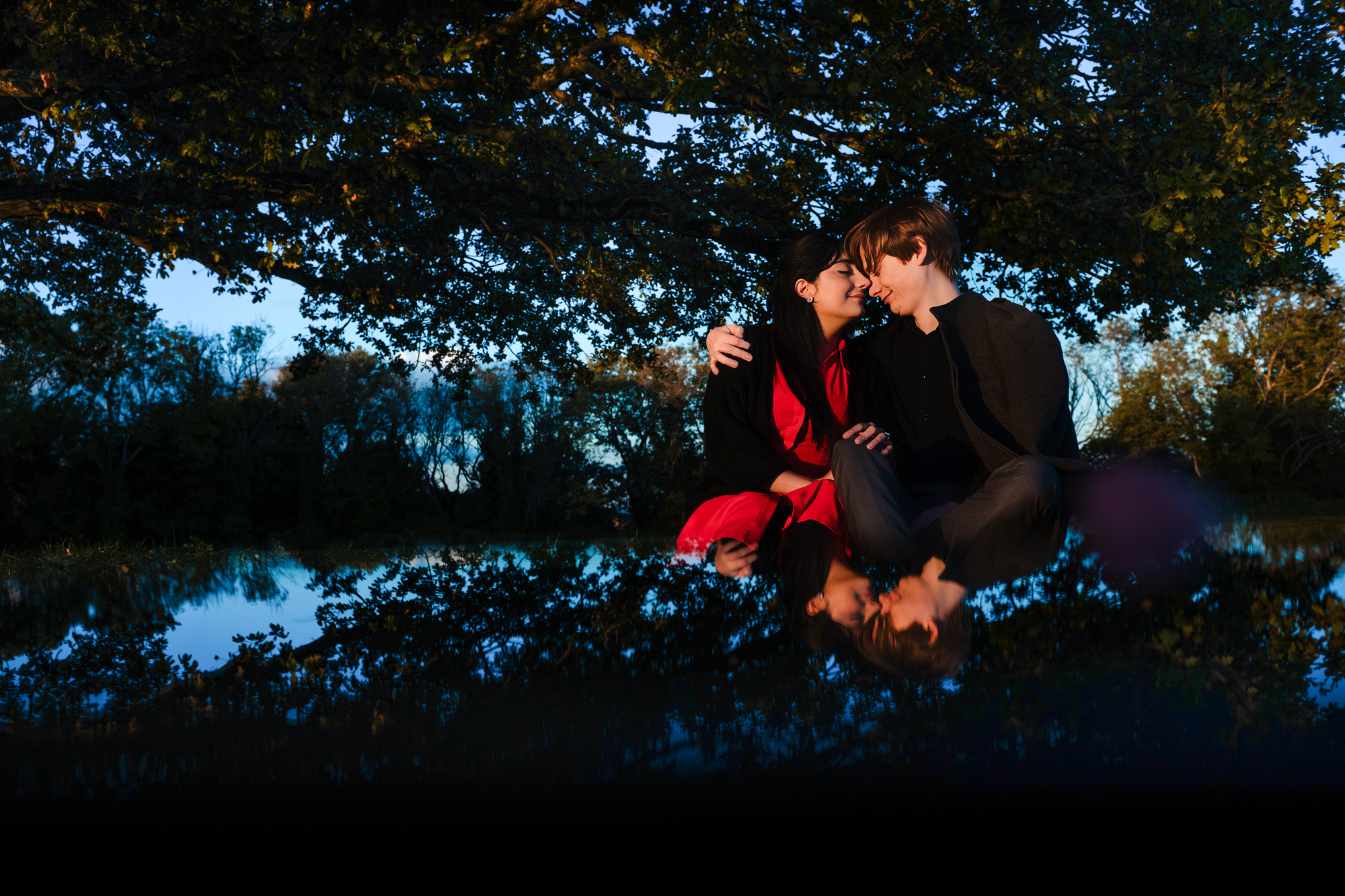 Couple sitting beneath oak tree with mirrored reflection during blue-hour Clifton engagement session.