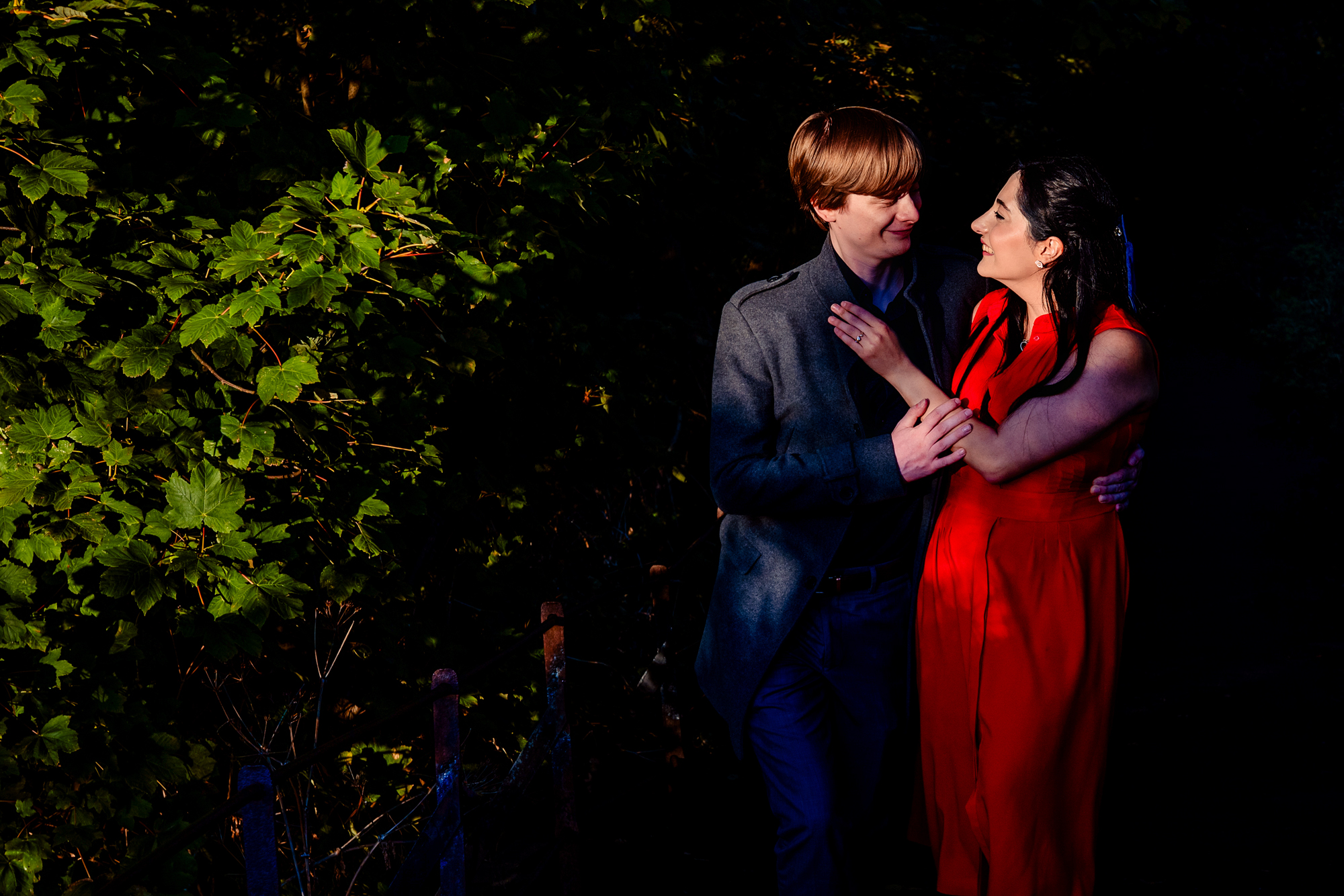 Engaged couple smiling at each other beside leafy path during golden-hour Clifton portrait session.