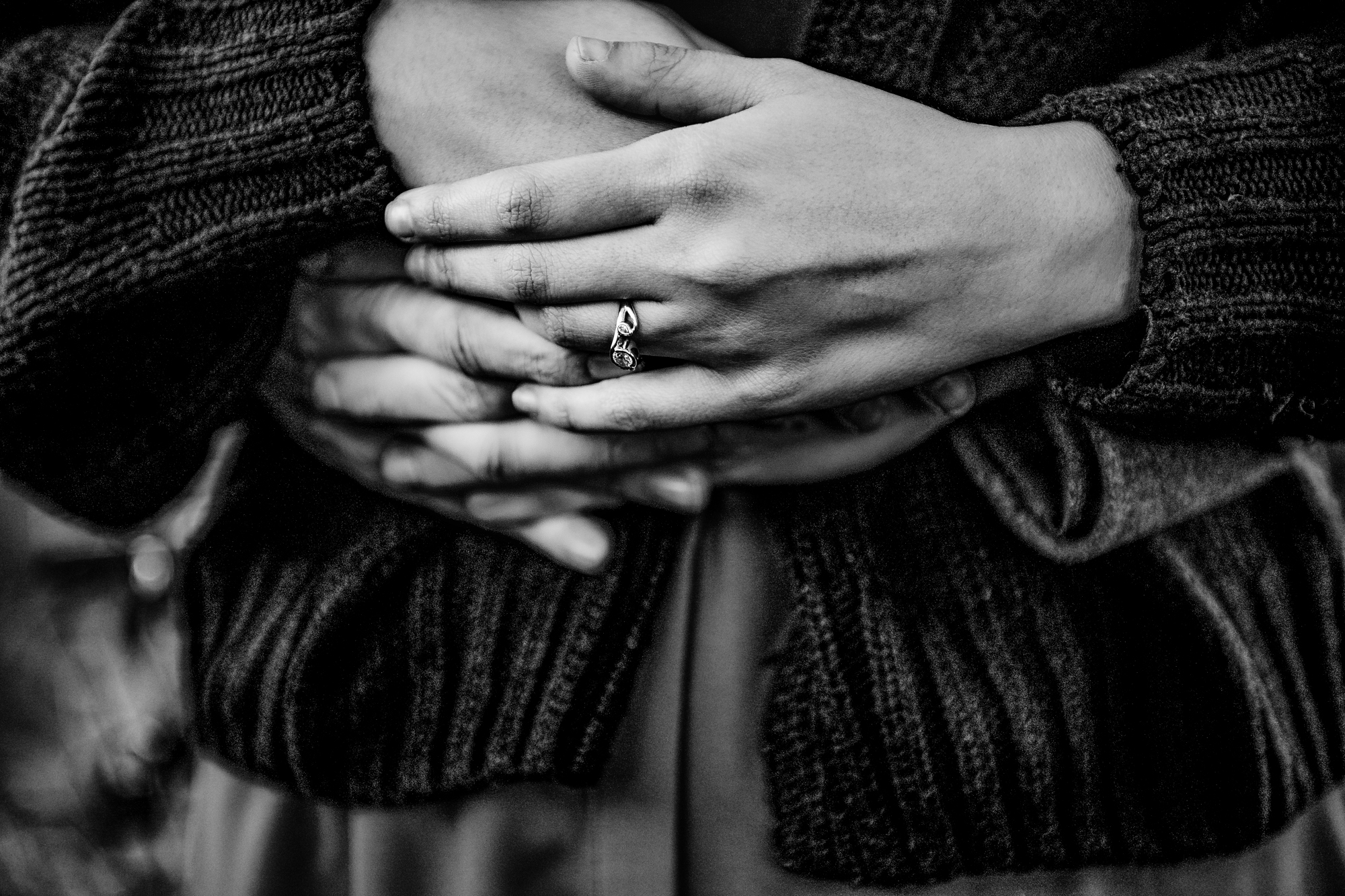 Black and white close-up of crossed arms with engagement ring during intimate couple portrait.