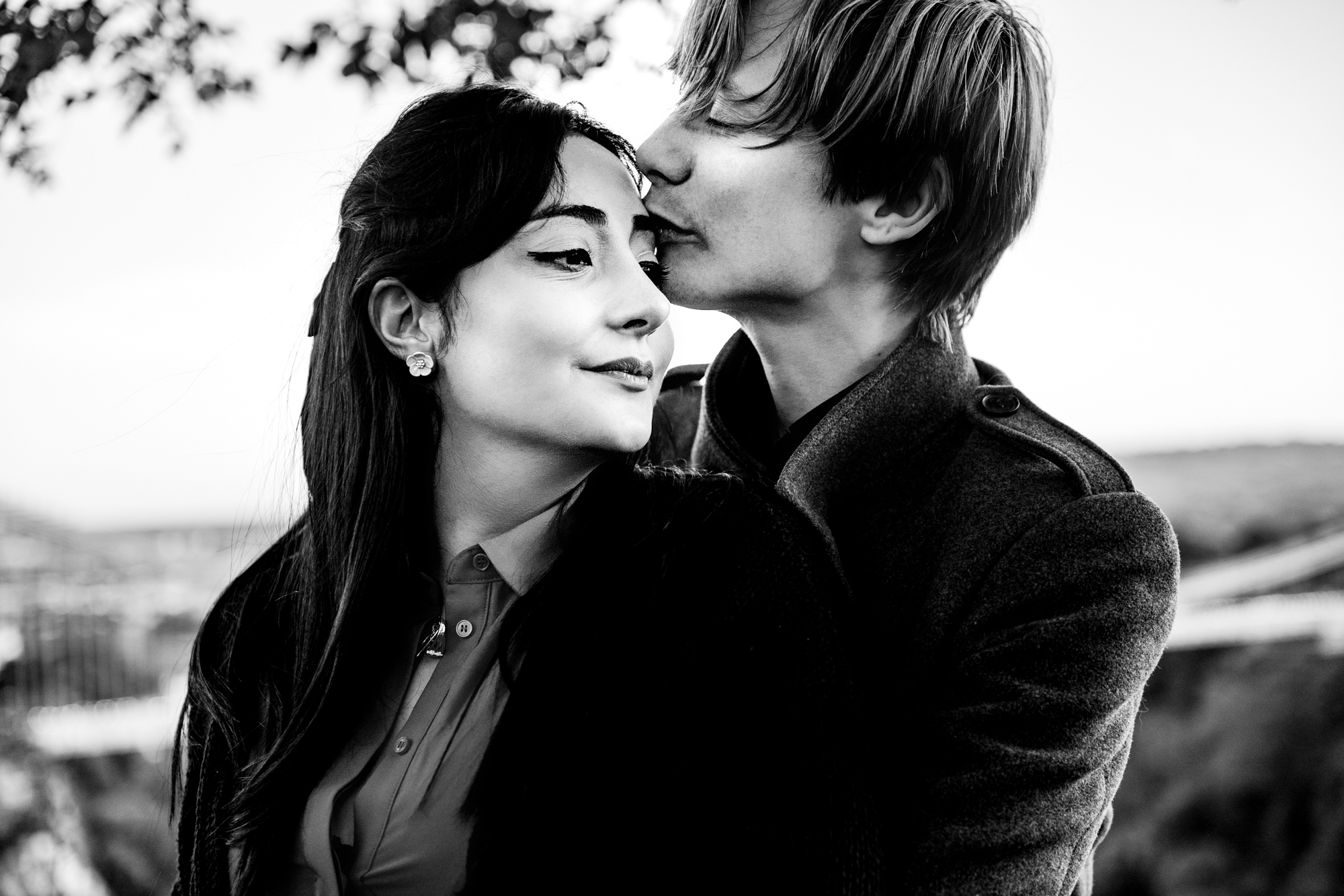 Black and white portrait of man kissing woman’s forehead during romantic Clifton engagement session.