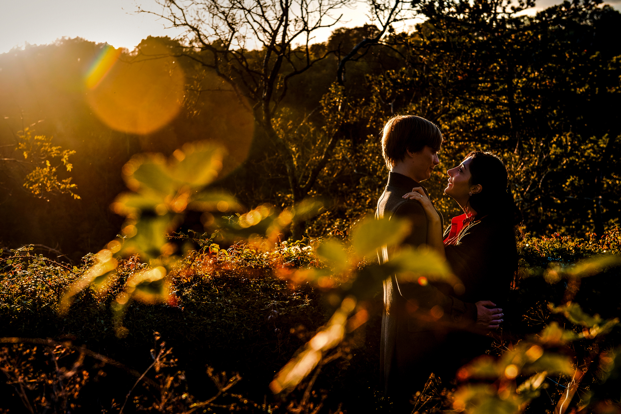 Couple embracing in glowing sunset light among autumn leaves during Clifton engagement session.