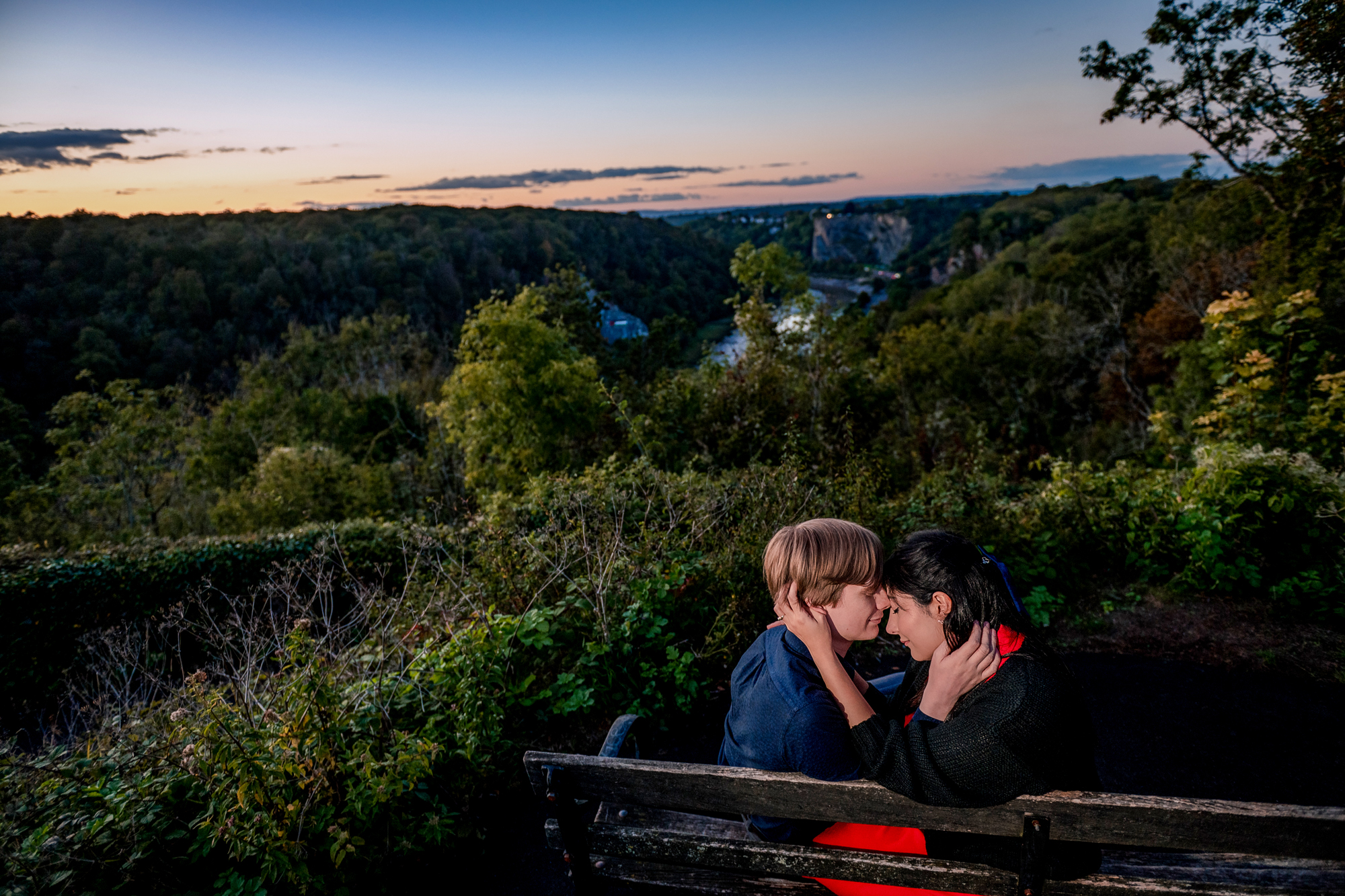 Couple sitting on bench overlooking Avon Gorge during blue-hour Clifton engagement session.