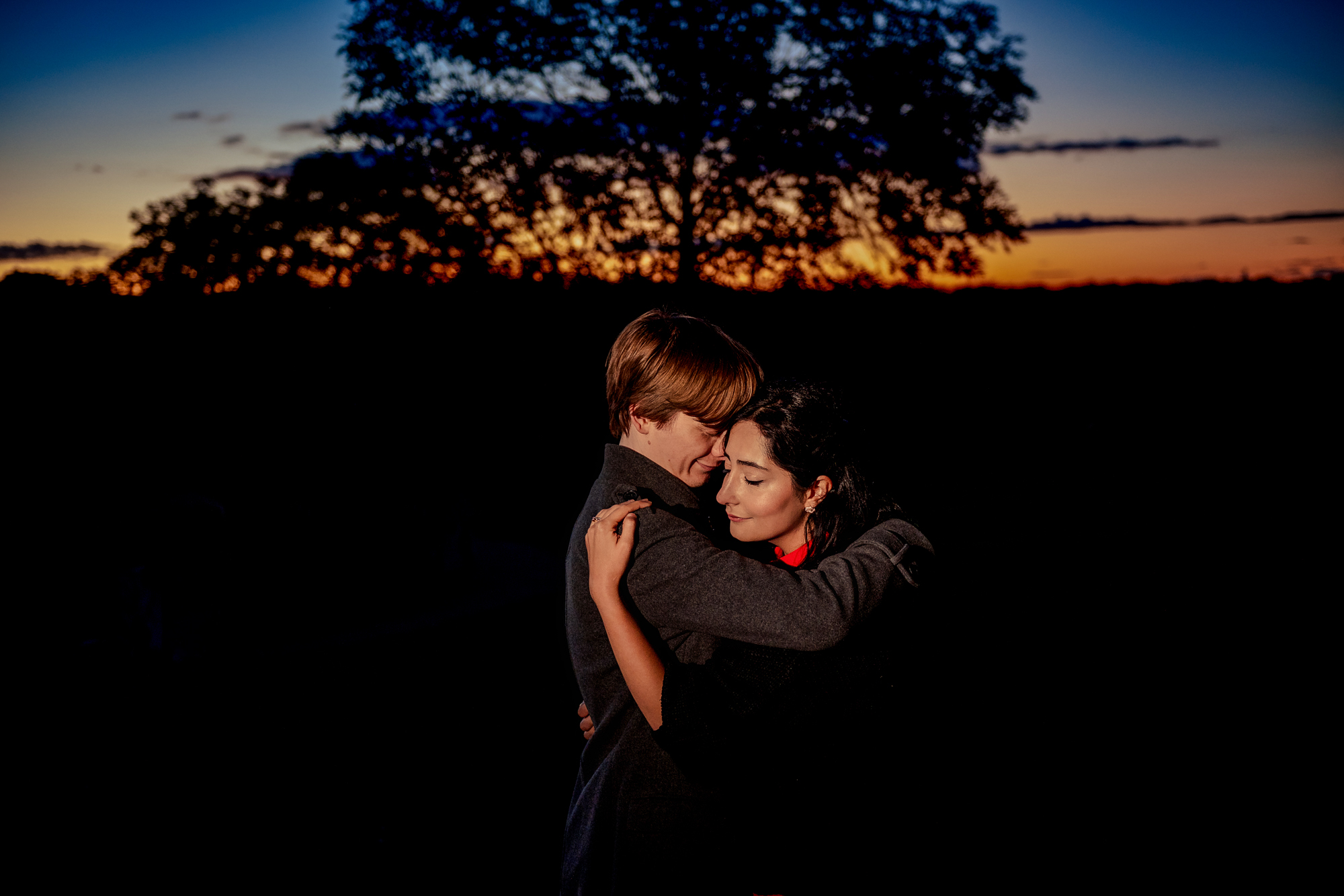 Couple embracing against deep sunset sky during dramatic evening engagement portrait.