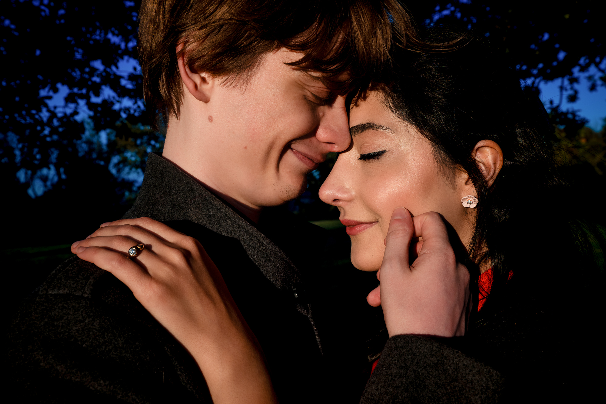 Intimate close-up portrait of engaged couple with closed eyes and soft evening light.