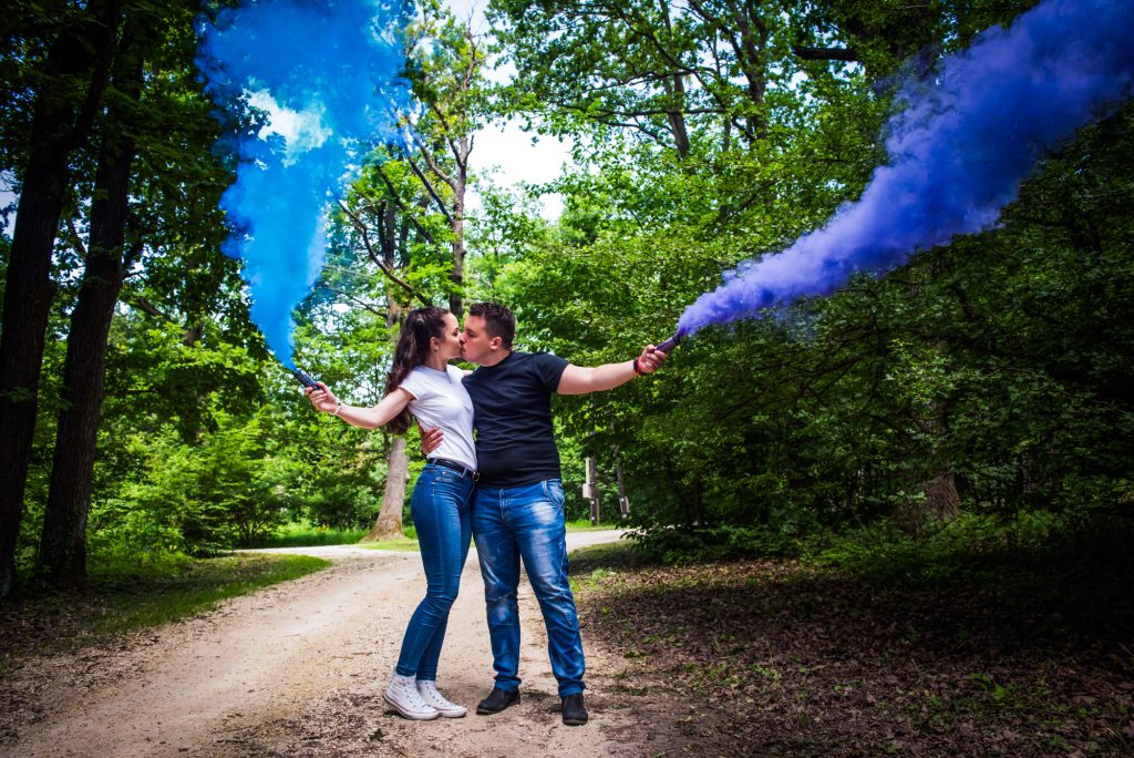 Couple kissing surrounded by coloured smoke during bold engagement session in woodland setting.