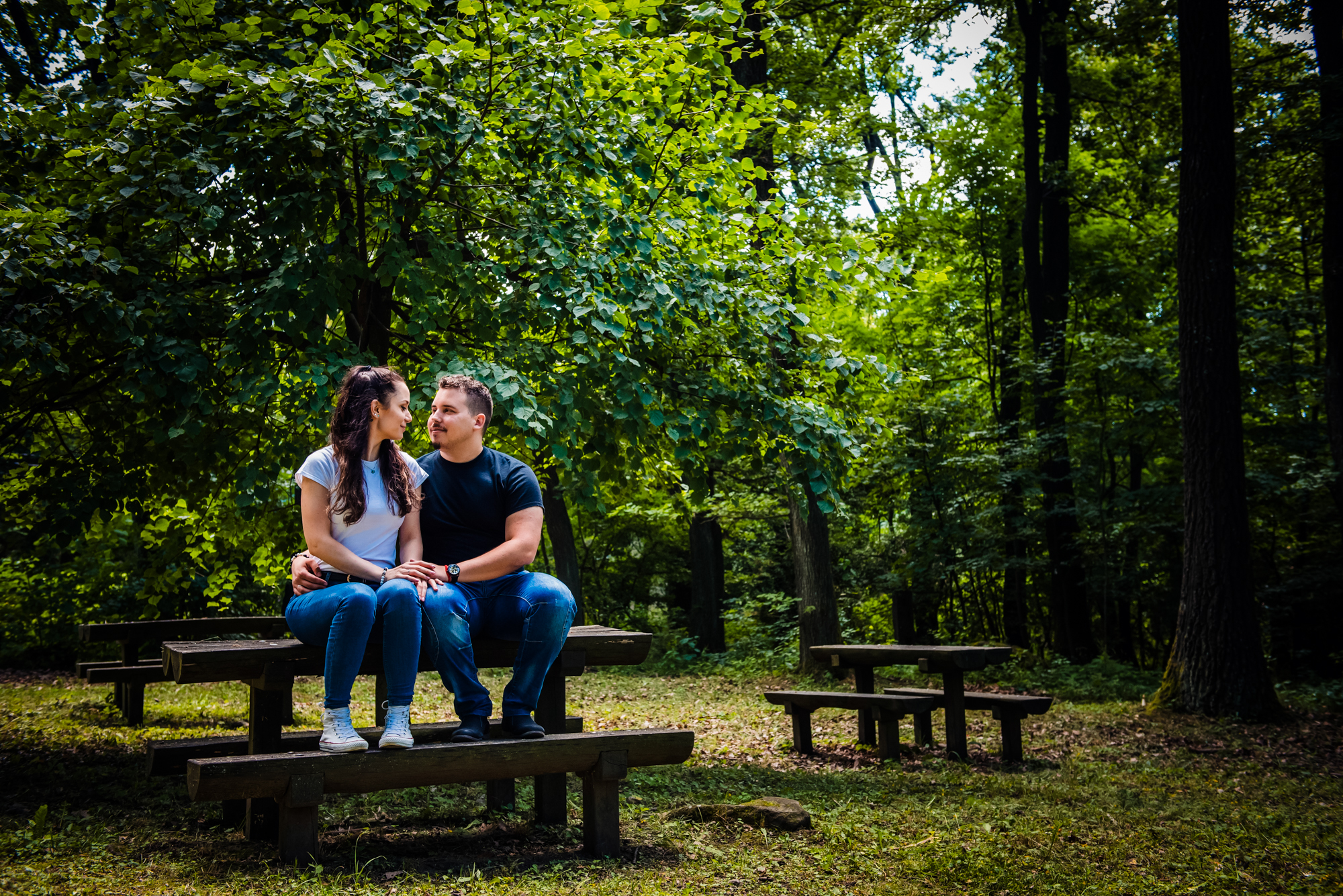 Couple sitting on picnic benches surrounded by greenery during calm forest engagement session in Hungary.