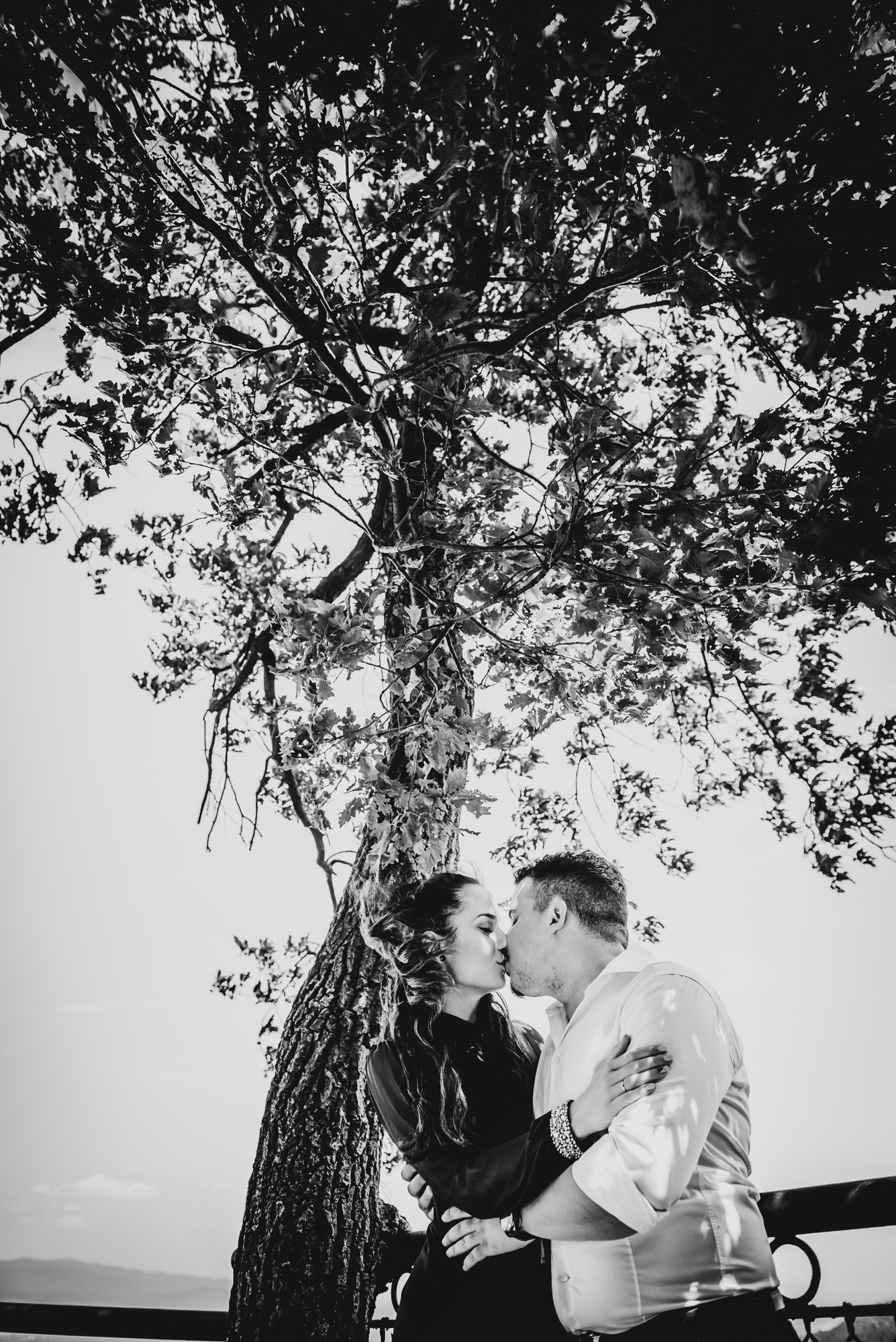Couple kissing under tree at scenic mountain viewpoint in Hungary.