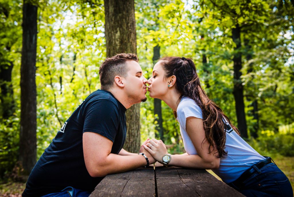 Couple leaning across picnic table about to kiss during playful forest engagement session in Hungary.