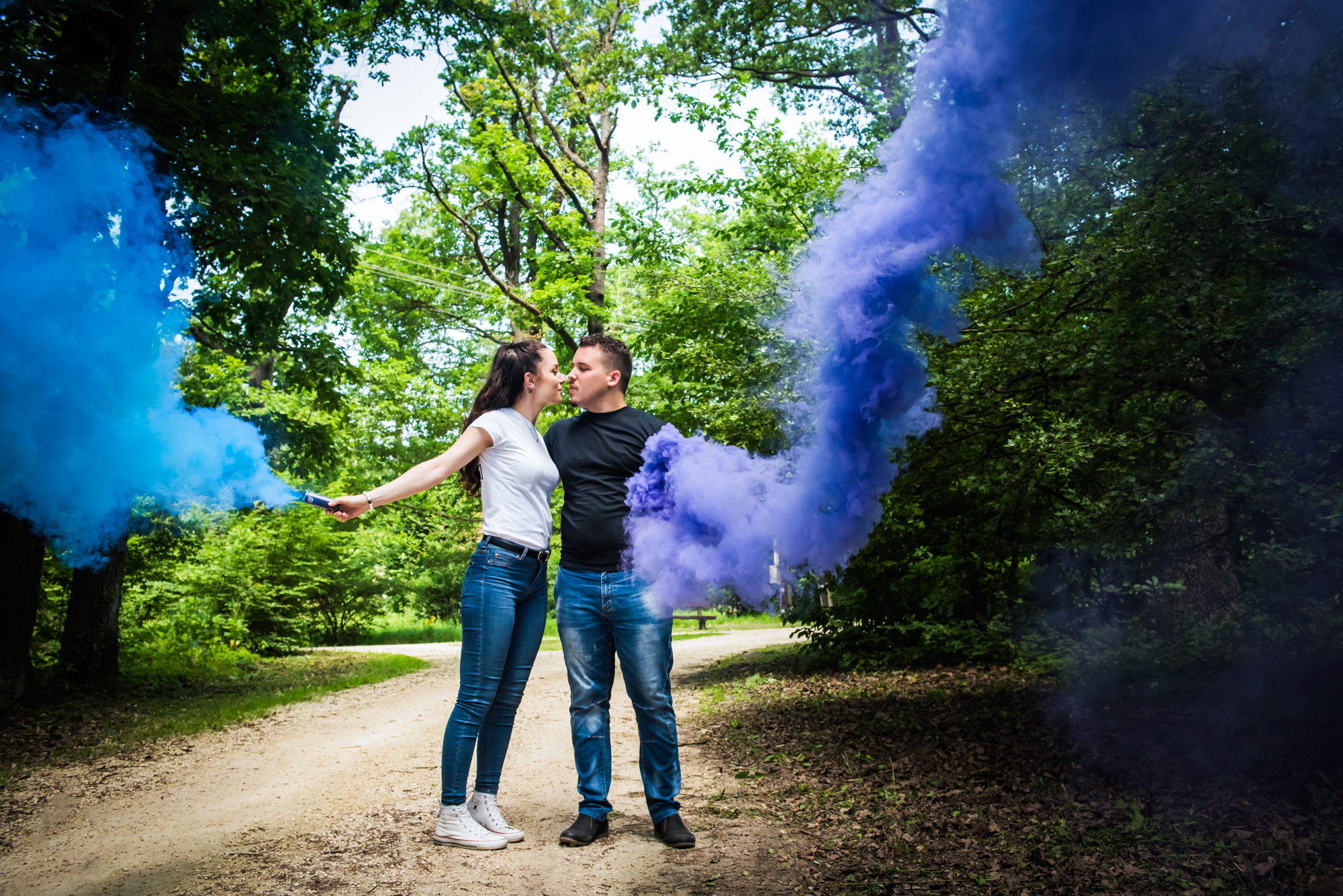 Couple walking playfully with coloured smoke bombs during relaxed engagement session in woodland.