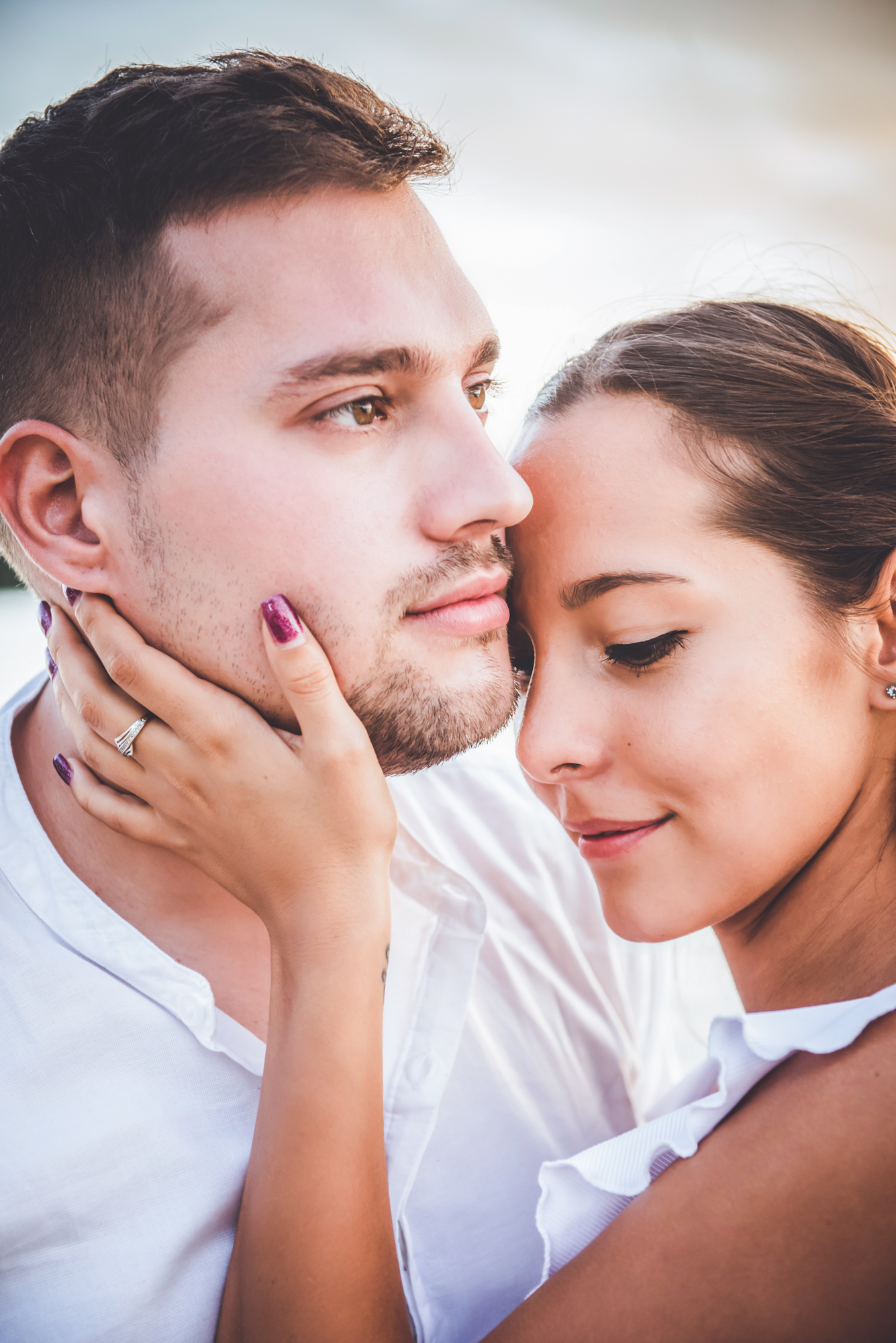 Woman gently holding partner’s face, close emotional engagement portrait at golden hour.