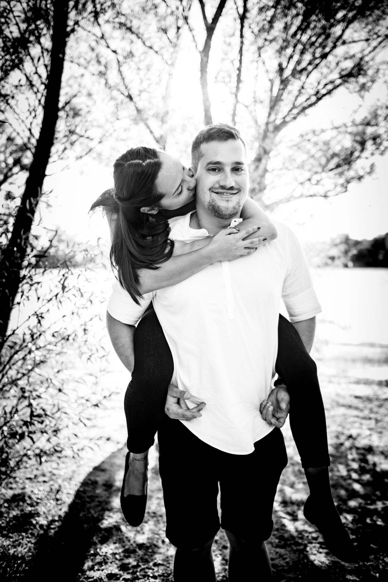 Black and white portrait of woman on partner’s back smiling during playful engagement session moment.
