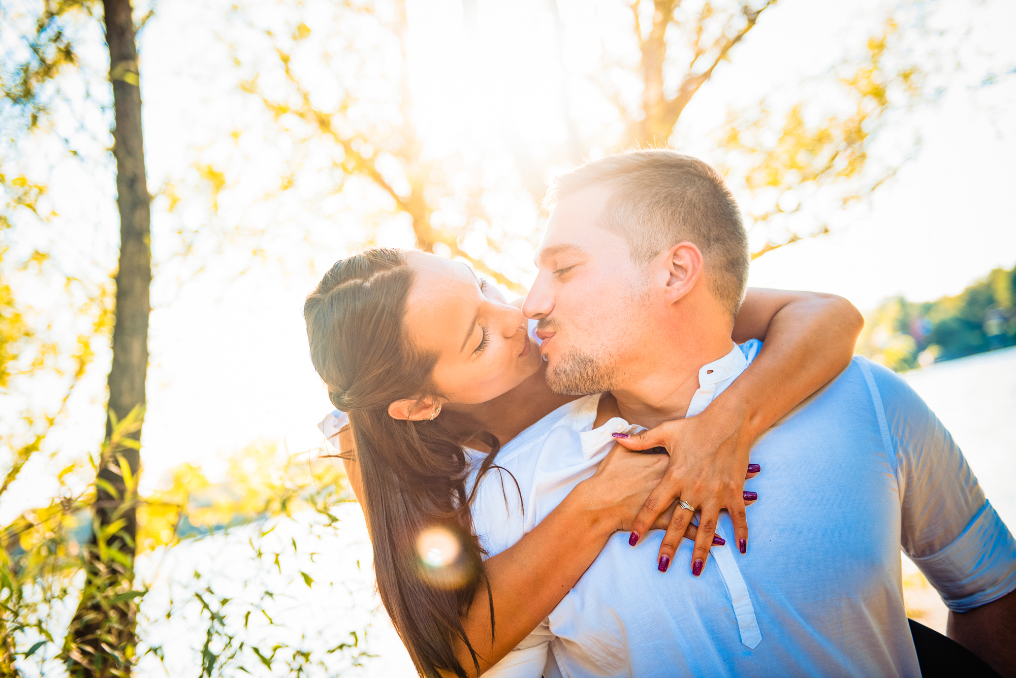 Couple kissing with warm golden sunlight and lens flare during Danube engagement session in Hungary.